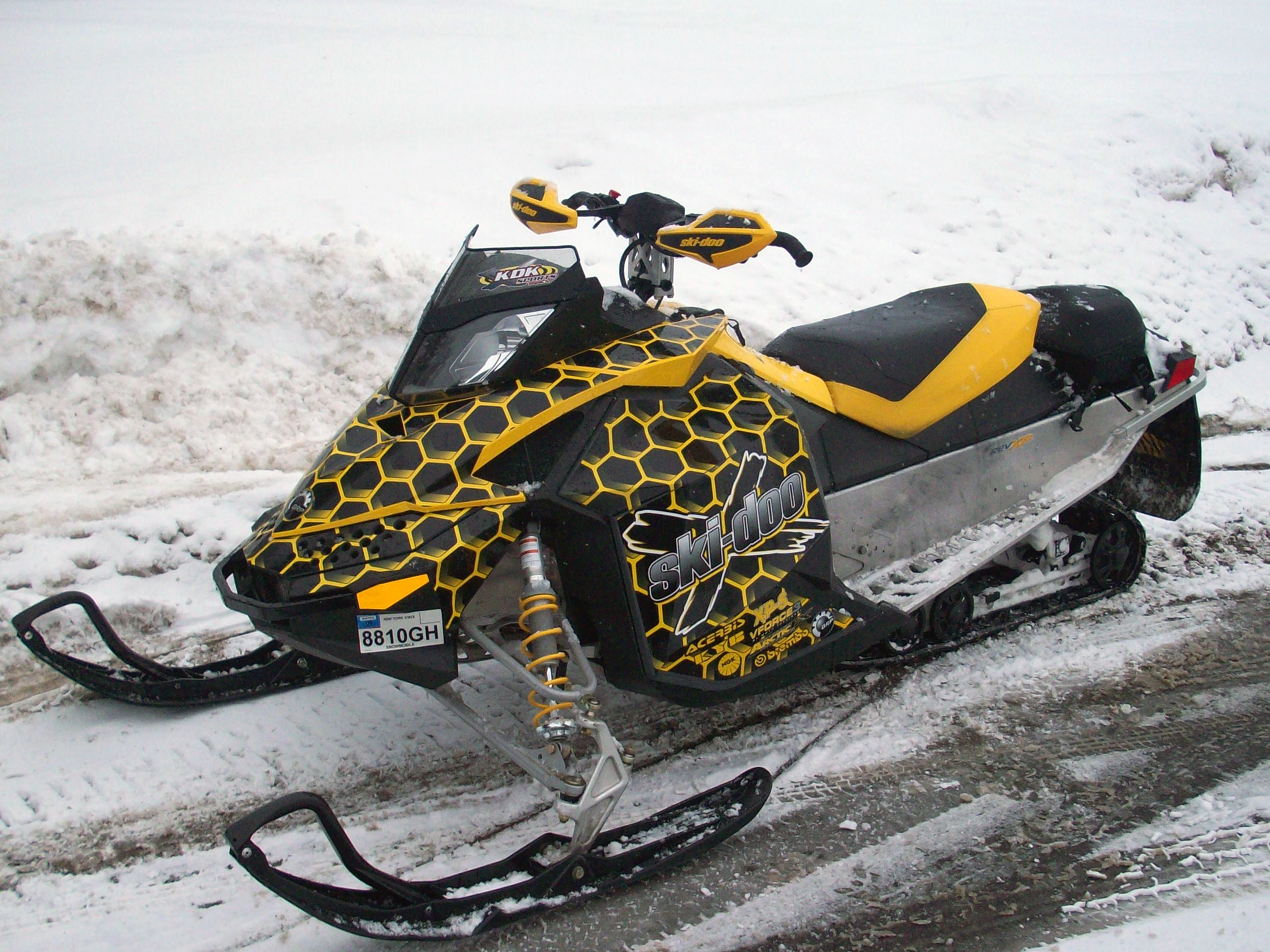 A Ski-Doo Rev XP snowmobile with a yellow and black Honeycomb pattern custom vinyl wrap.