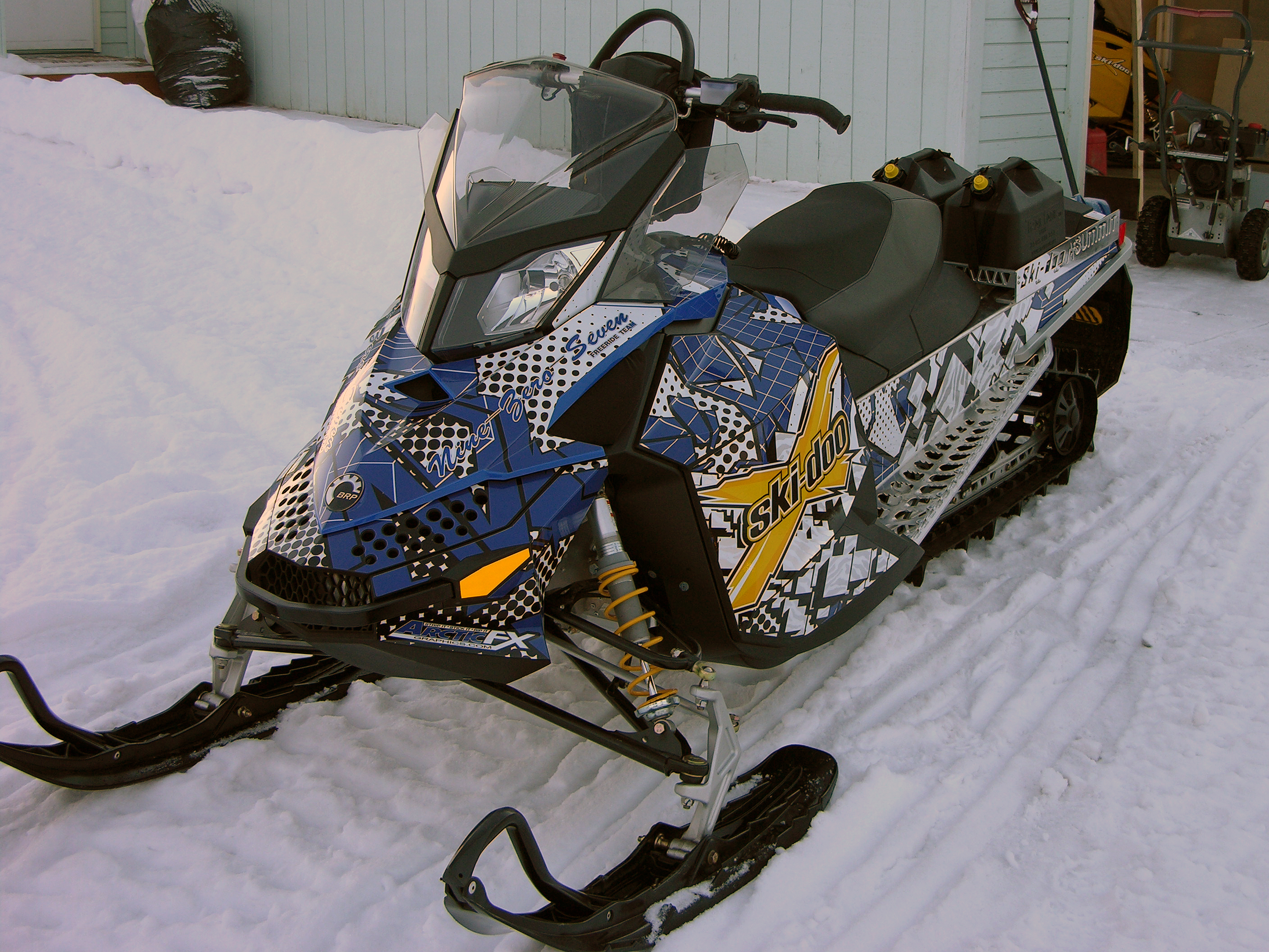 A Ski-Doo Rev XP snowmobile with a blue, white, and black Instinct custom vinyl wrap.