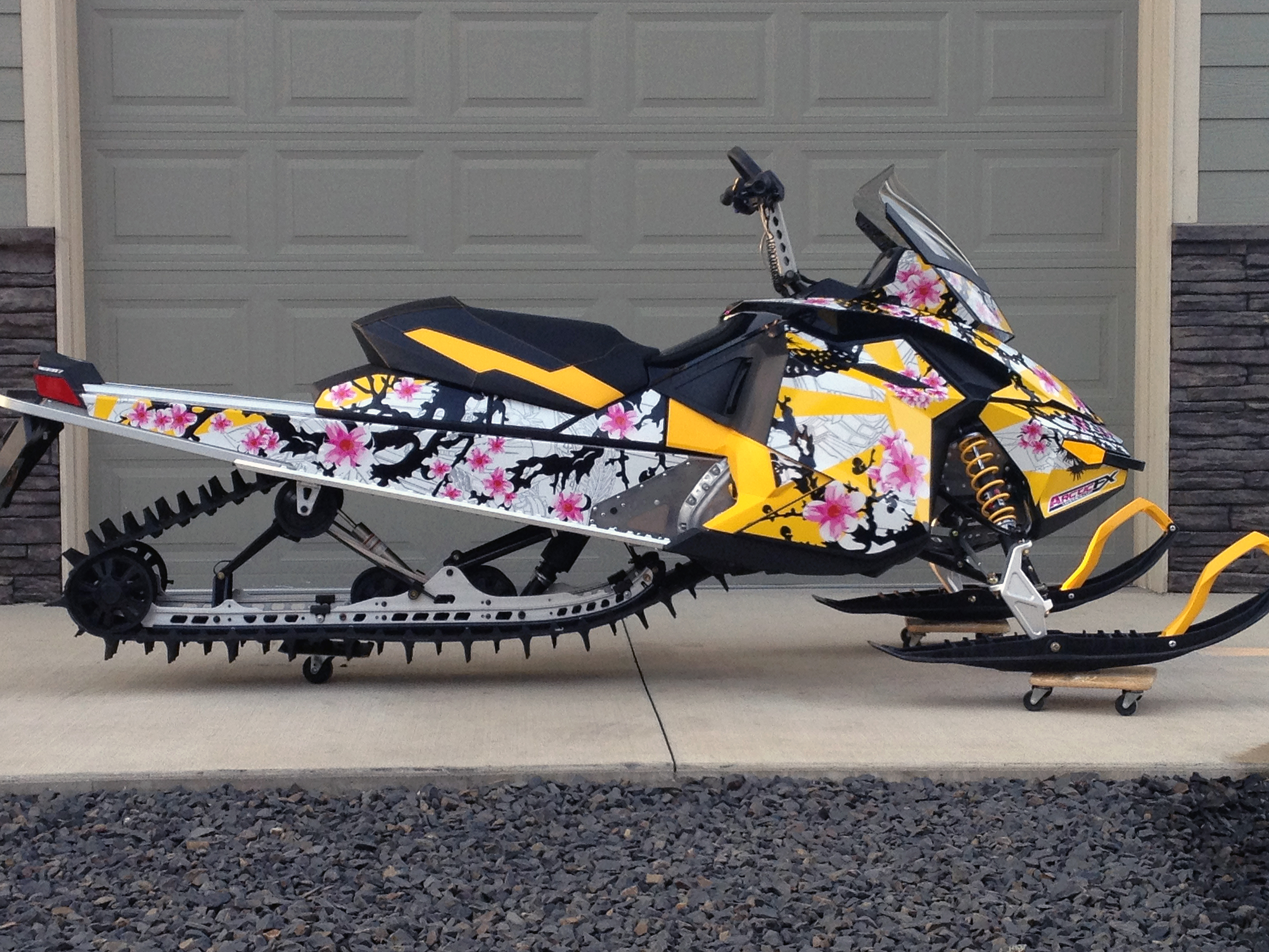 A Ski-Doo Rev XP snowmobile with a yellow, pink, and white Last Resort custom vinyl wrap.