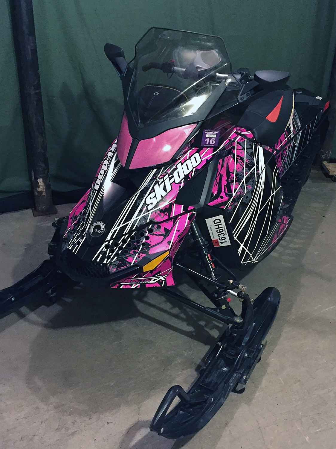 A Ski-Doo Rev XP snowmobile with a pink, white, and black Linearality custom vinyl wrap.
