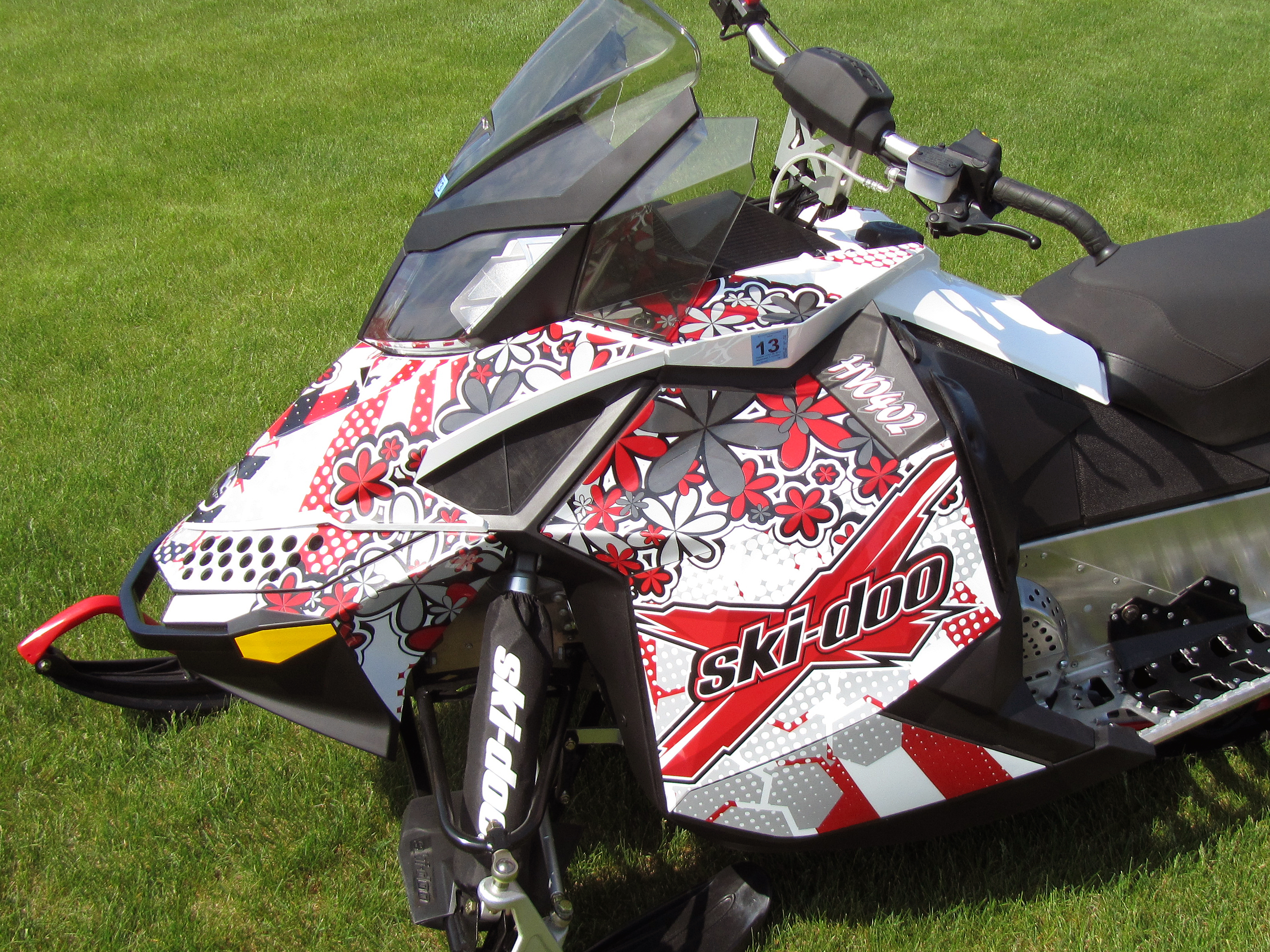 A Ski-Doo Rev XP snowmobile with a white, black, and red flowers Monica custom vinyl wrap.