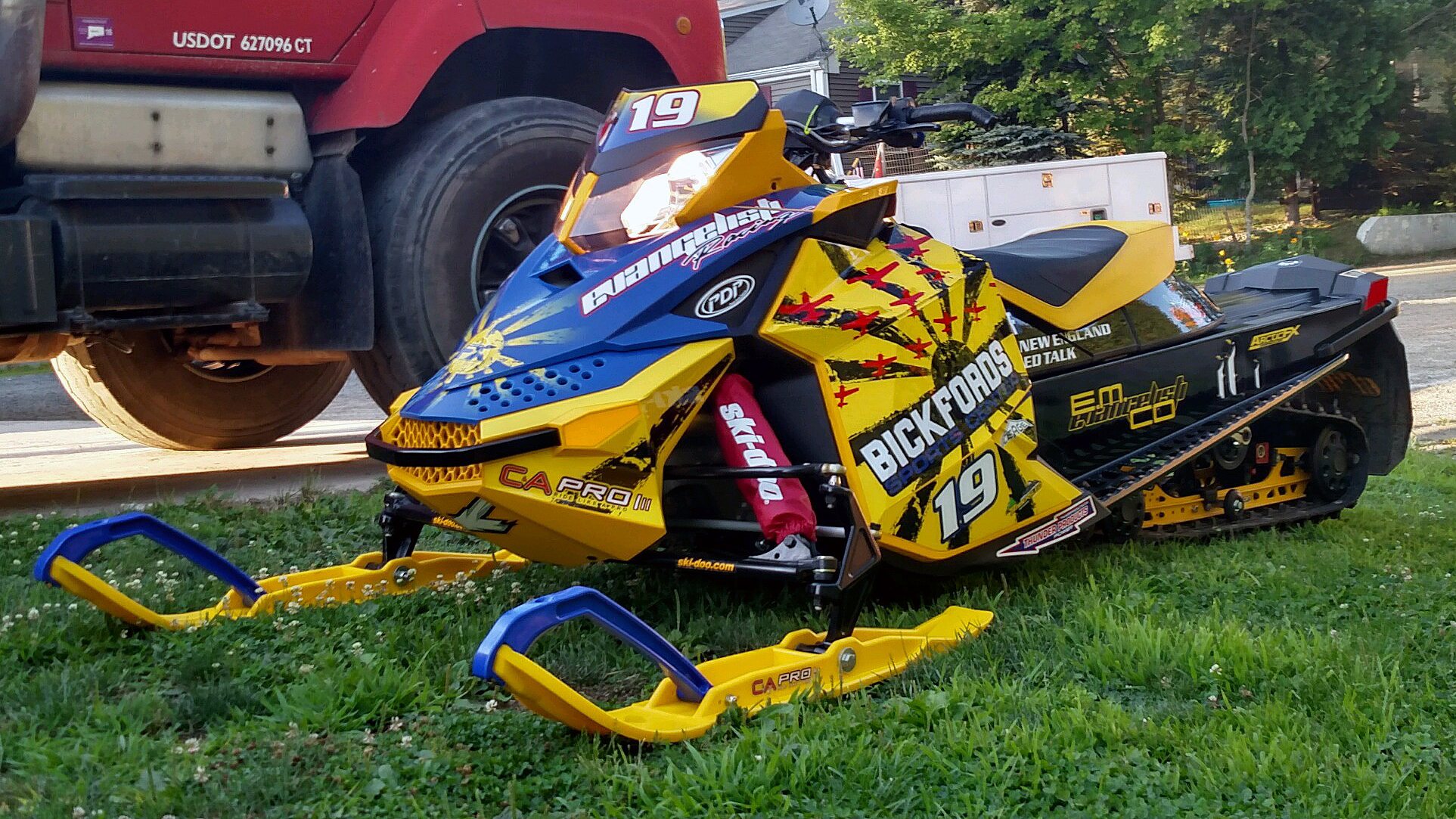A Ski-Doo Rev XP snowmobile with a yellow, blue, and red Rising Sun custom vinyl wrap.