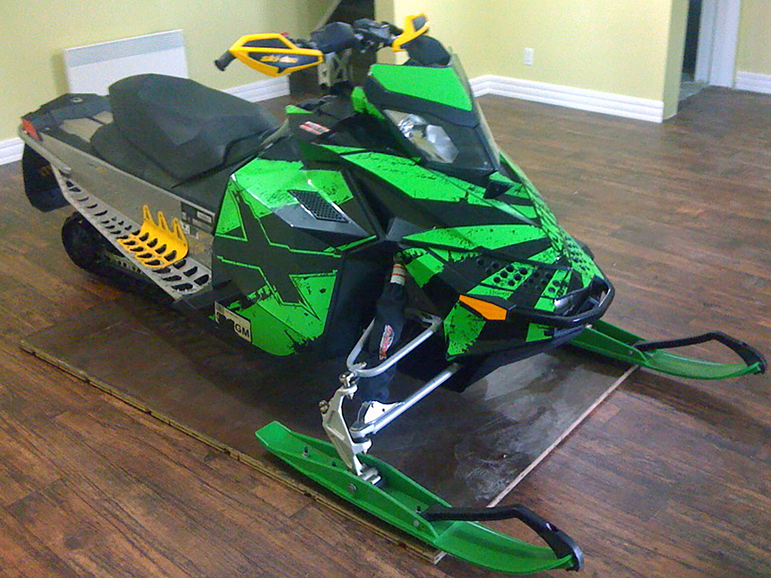 A Ski-Doo Rev XP snowmobile with a lime and black Rising Sun custom vinyl wrap.