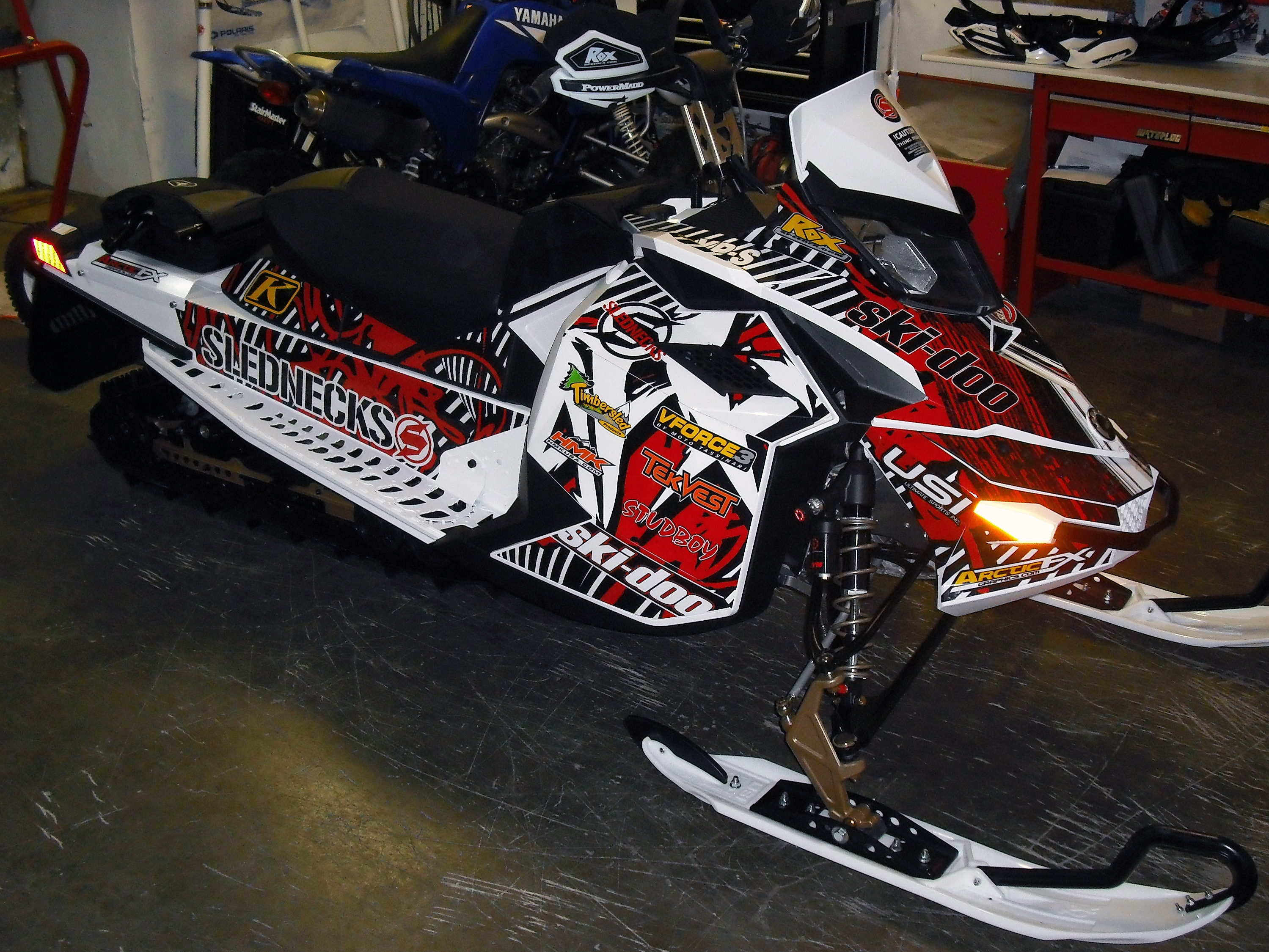 A Ski-Doo Rev XP snowmobile with a white, black, and red Scrib custom vinyl wrap.