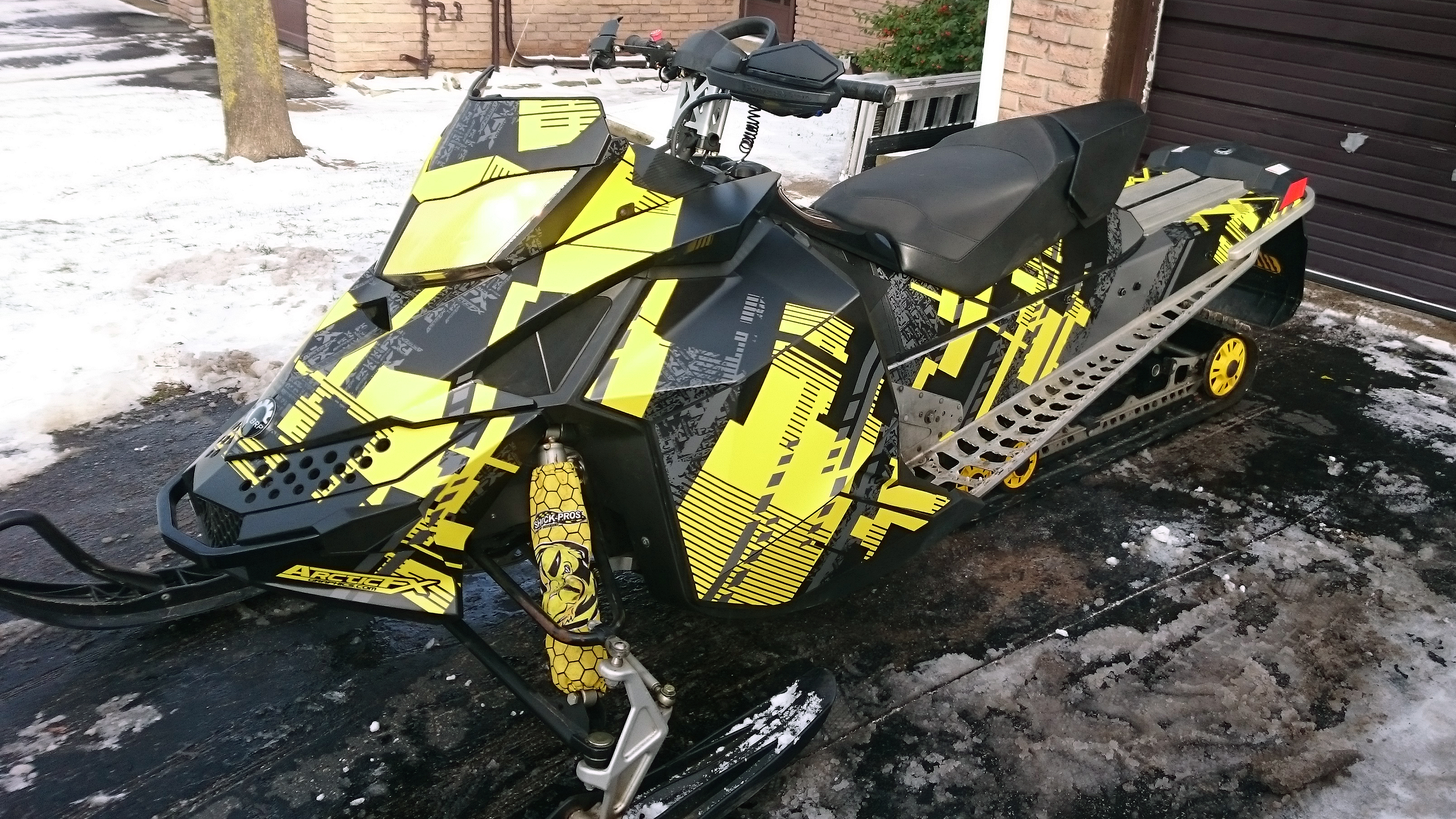 A Ski-Doo Rev XP snowmobile with a yellow and black Swerve City custom vinyl wrap.