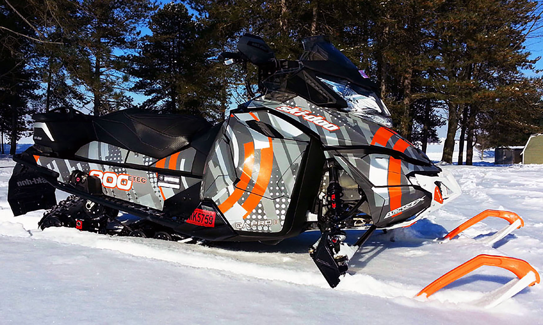 A Ski-Doo Rev XS snowmobile with a orange, gray, and white Arc Reactor custom vinyl wrap.