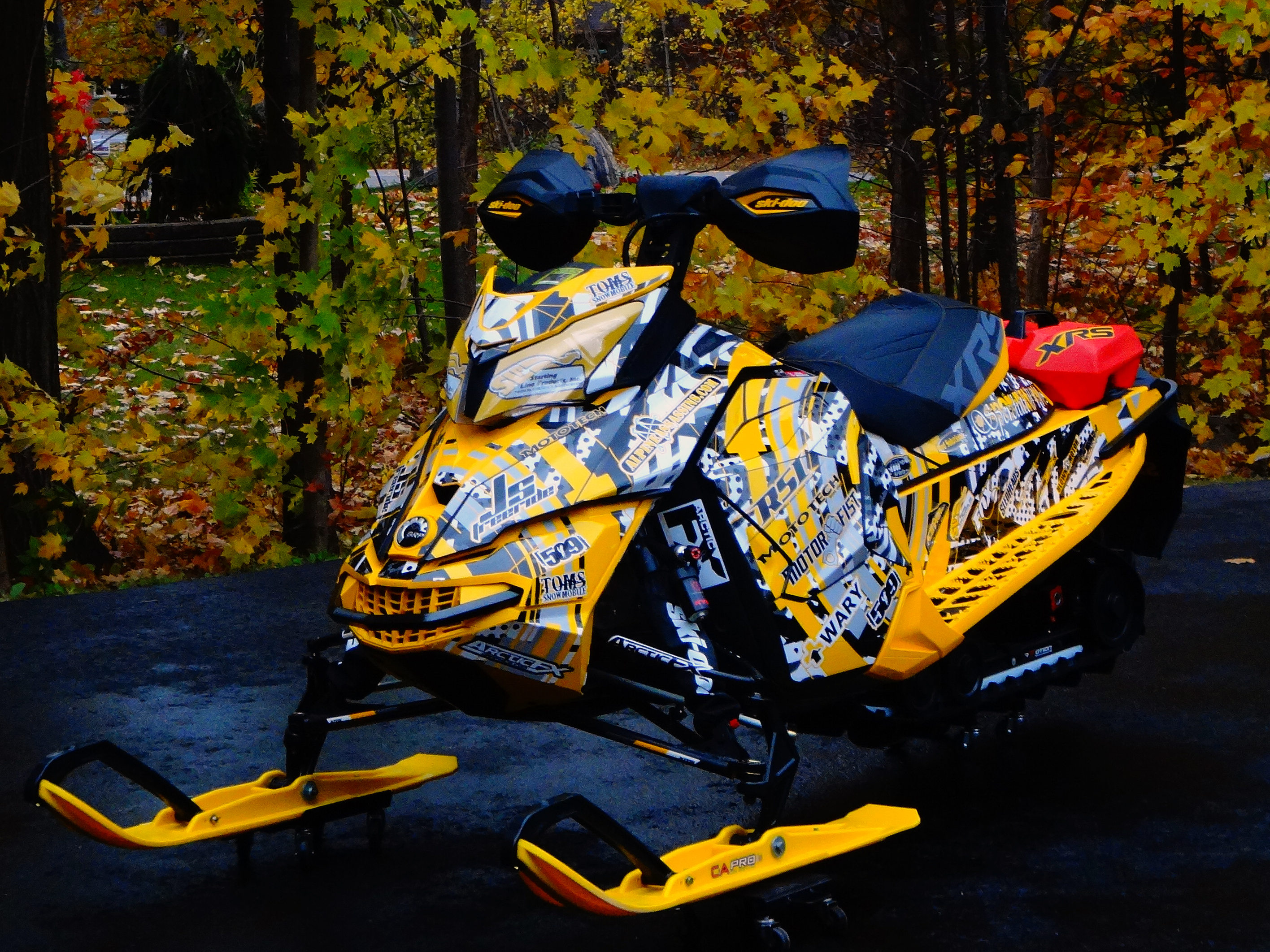 A Ski-Doo Rev XS snowmobile with a yellow, black, and white Kelley Arc Reactor custom vinyl wrap.