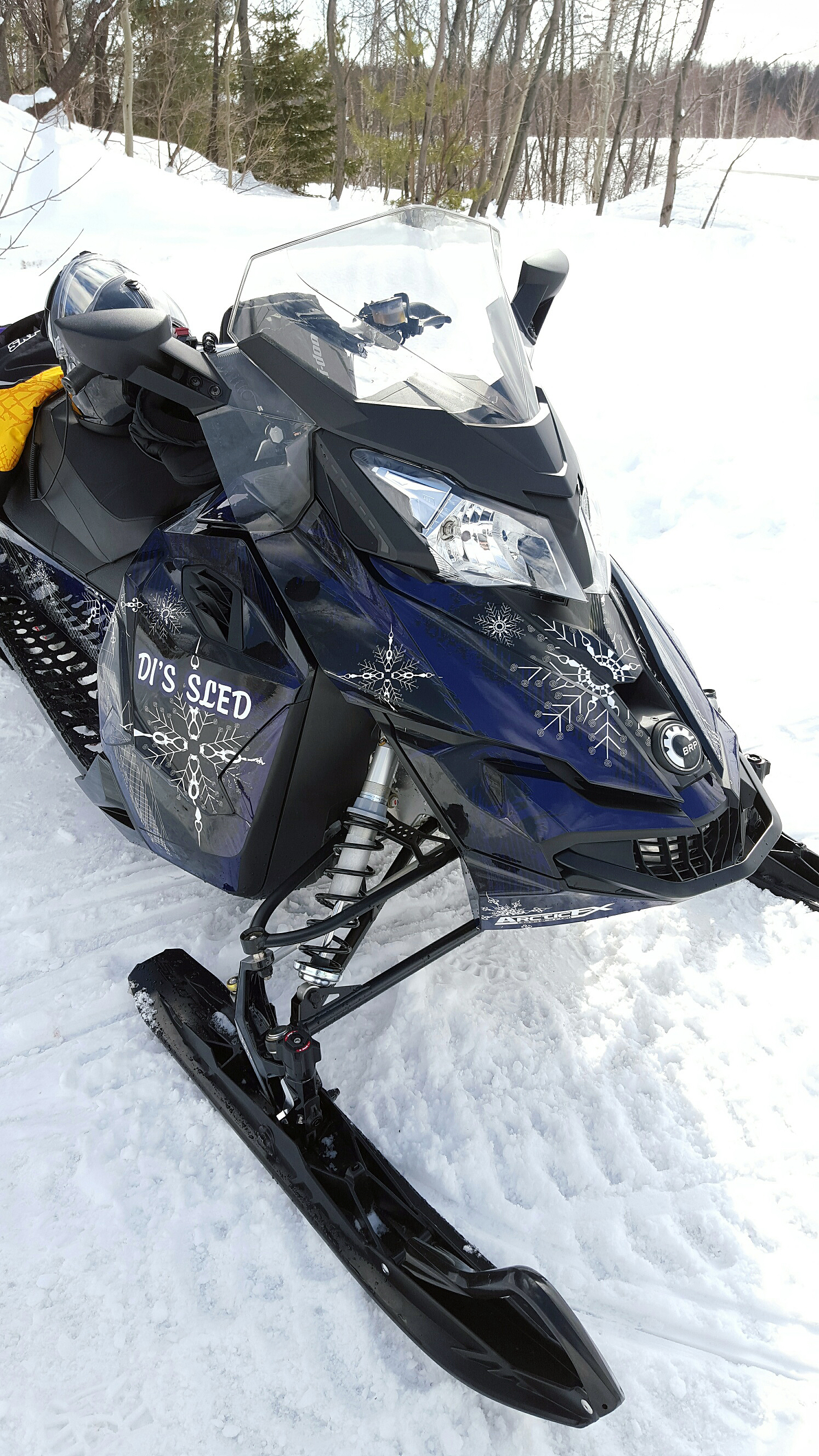 A Ski-Doo Rev XS snowmobile with a navy, black, and white Snow Storm custom vinyl wrap.