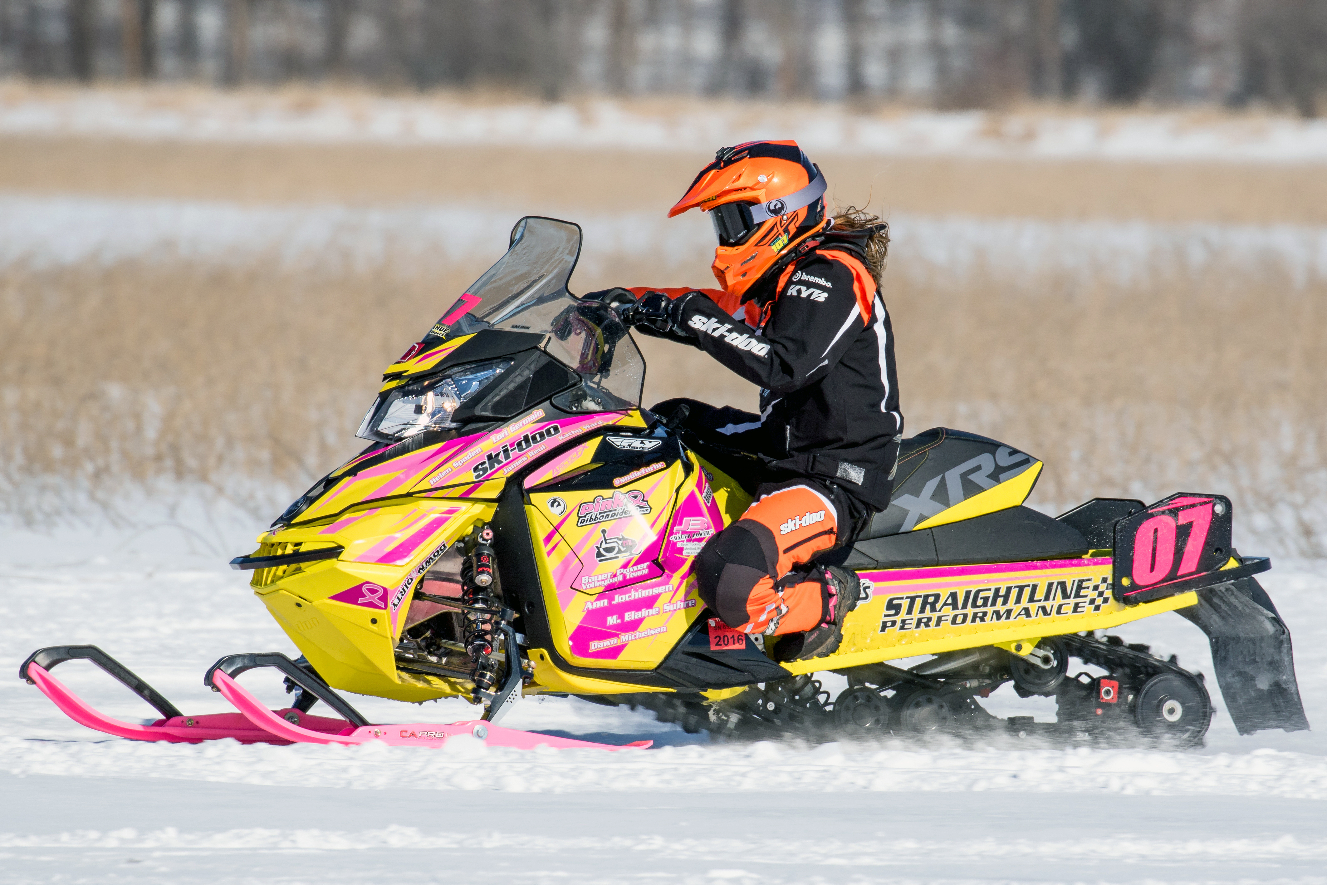 A Ski-Doo Rev XS snowmobile with a yellow, pink, and black StraightLine racing custom vinyl wrap.