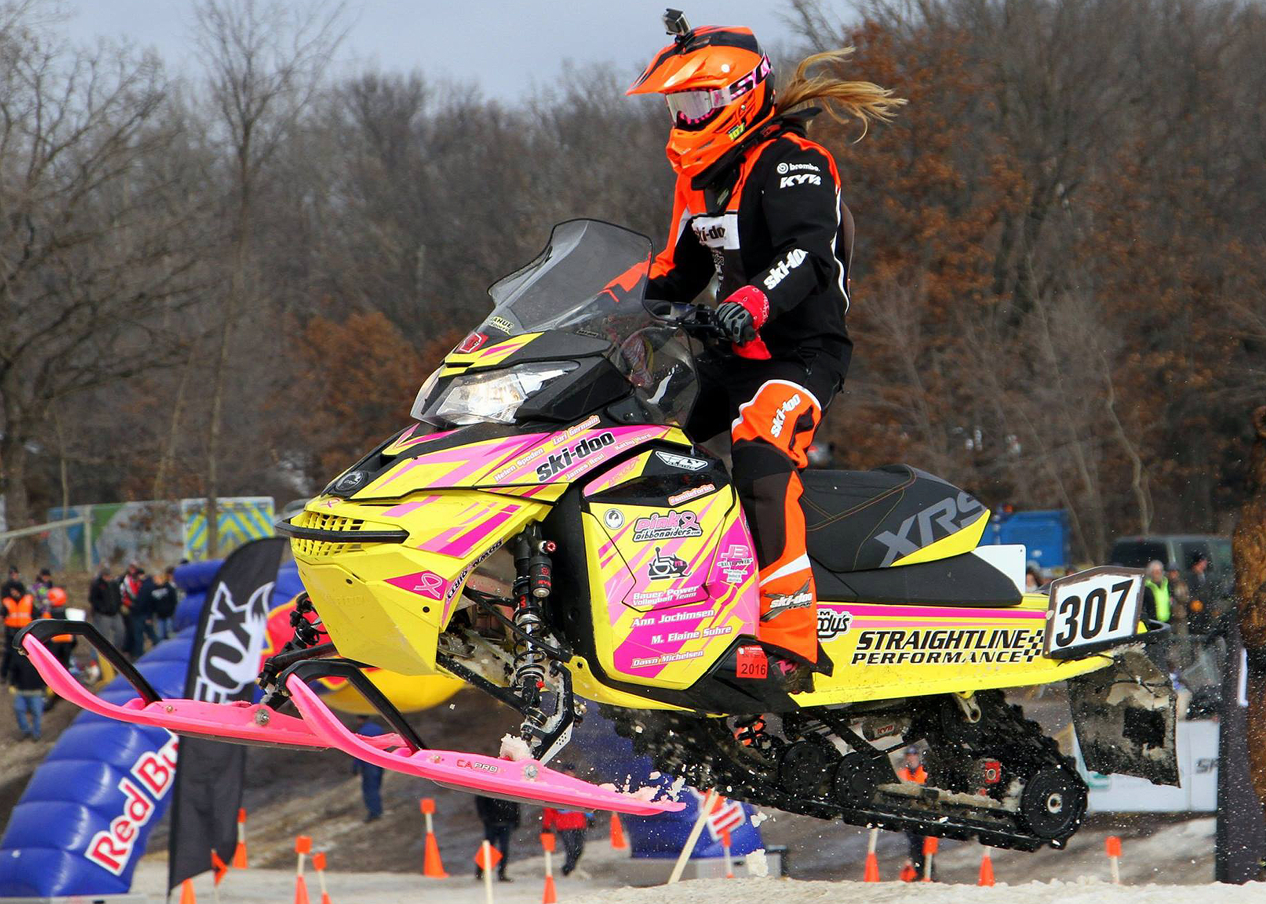 A Ski-Doo Rev XS snowmobile with a yellow, pink, and black StraightLine racing custom vinyl wrap.