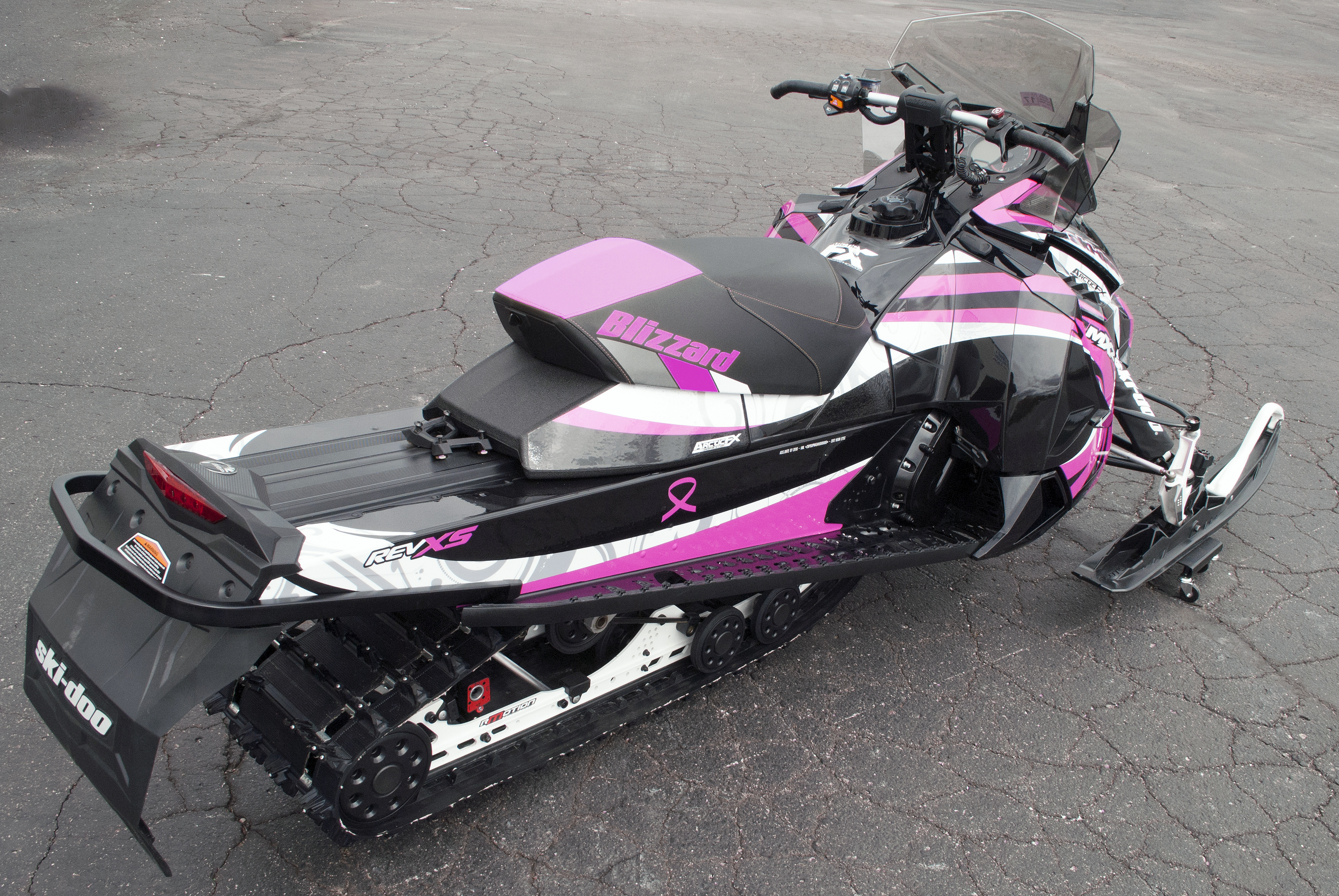 A Ski-Doo Rev XS snowmobile with a white, pink, and black Surge custom vinyl wrap.
