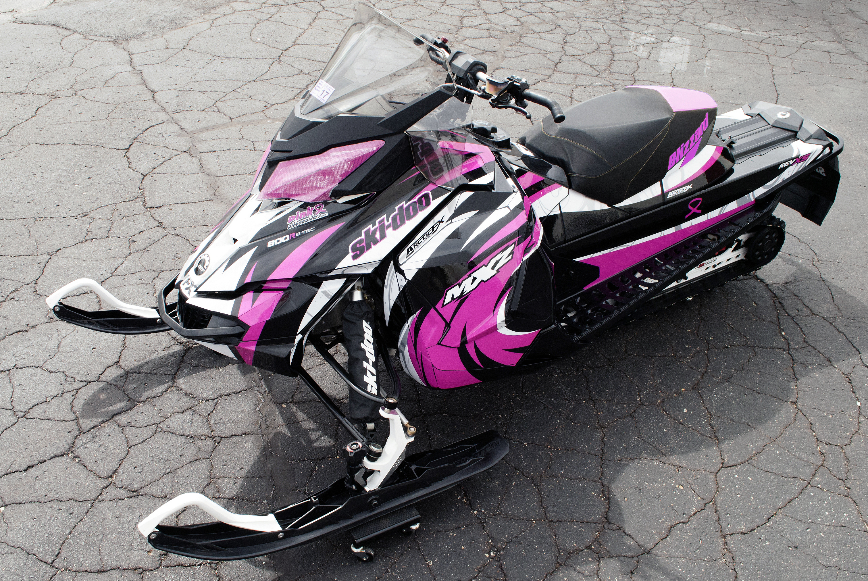 A Ski-Doo Rev XS snowmobile with a white, pink, and black Surge custom vinyl wrap.