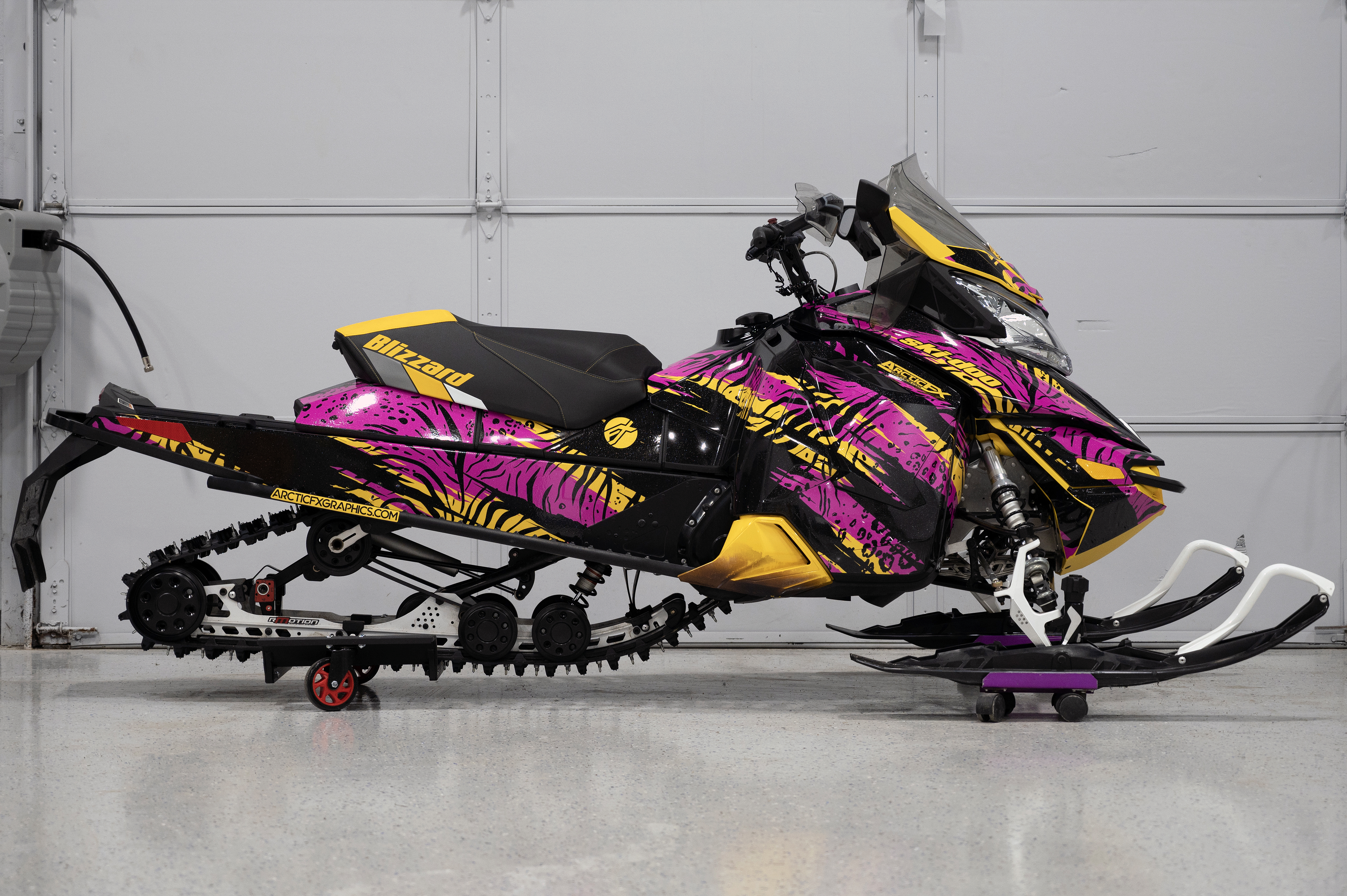 A Ski-Doo Rev XS snowmobile with a yellow, pink, and black Threshold custom vinyl wrap.
