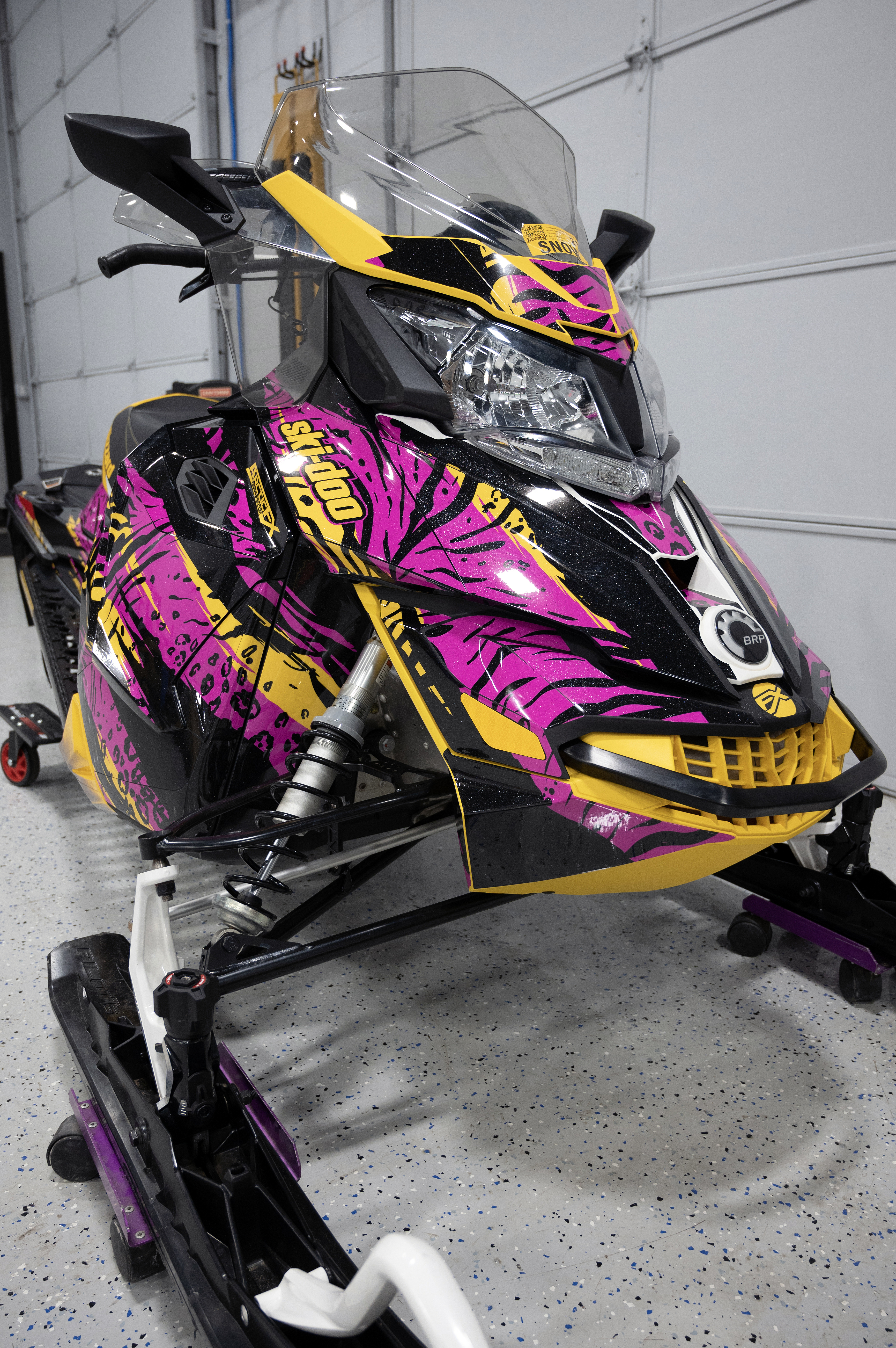 A Ski-Doo Rev XS snowmobile with a yellow, pink, and black Threshold custom vinyl wrap.