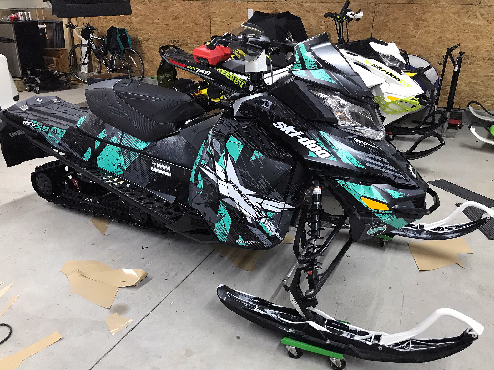 A Ski-Doo Rev XS snowmobile with a aqua, gray, and black Wartorn custom vinyl wrap.