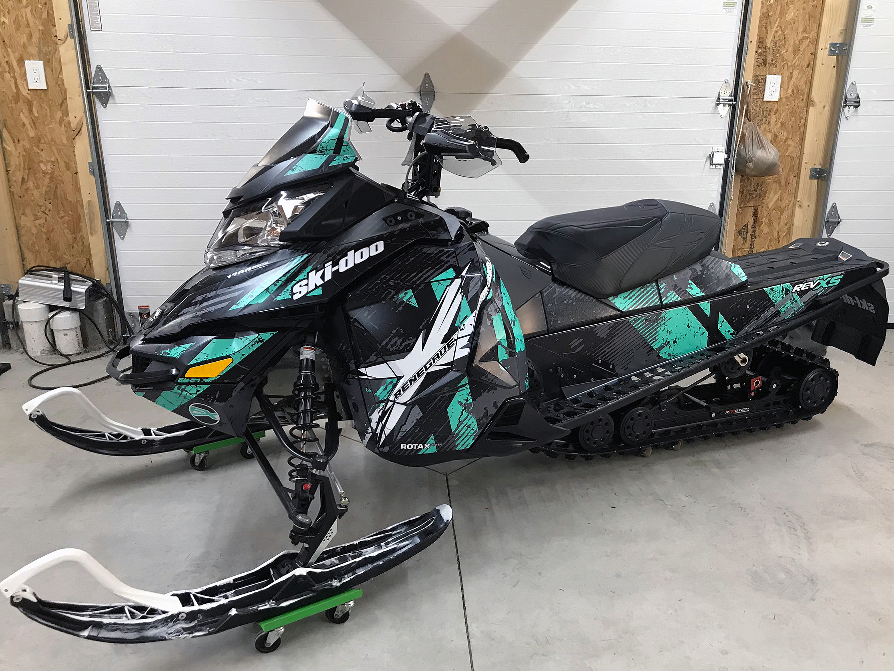 A Ski-Doo Rev XS snowmobile with a aqua, gray, and black Wartorn custom vinyl wrap.