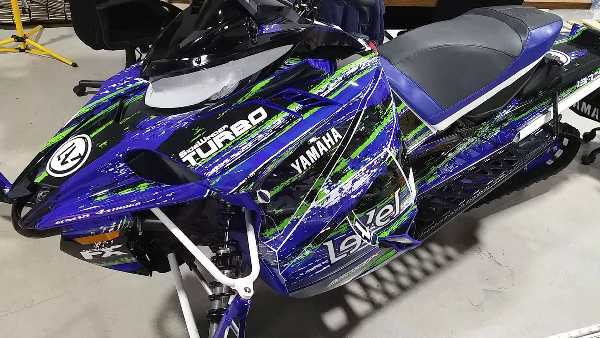 A Yamaha Sidewinder snowmobile with a blue, black, and green grunge lightning Infused custom vinyl wrap.
