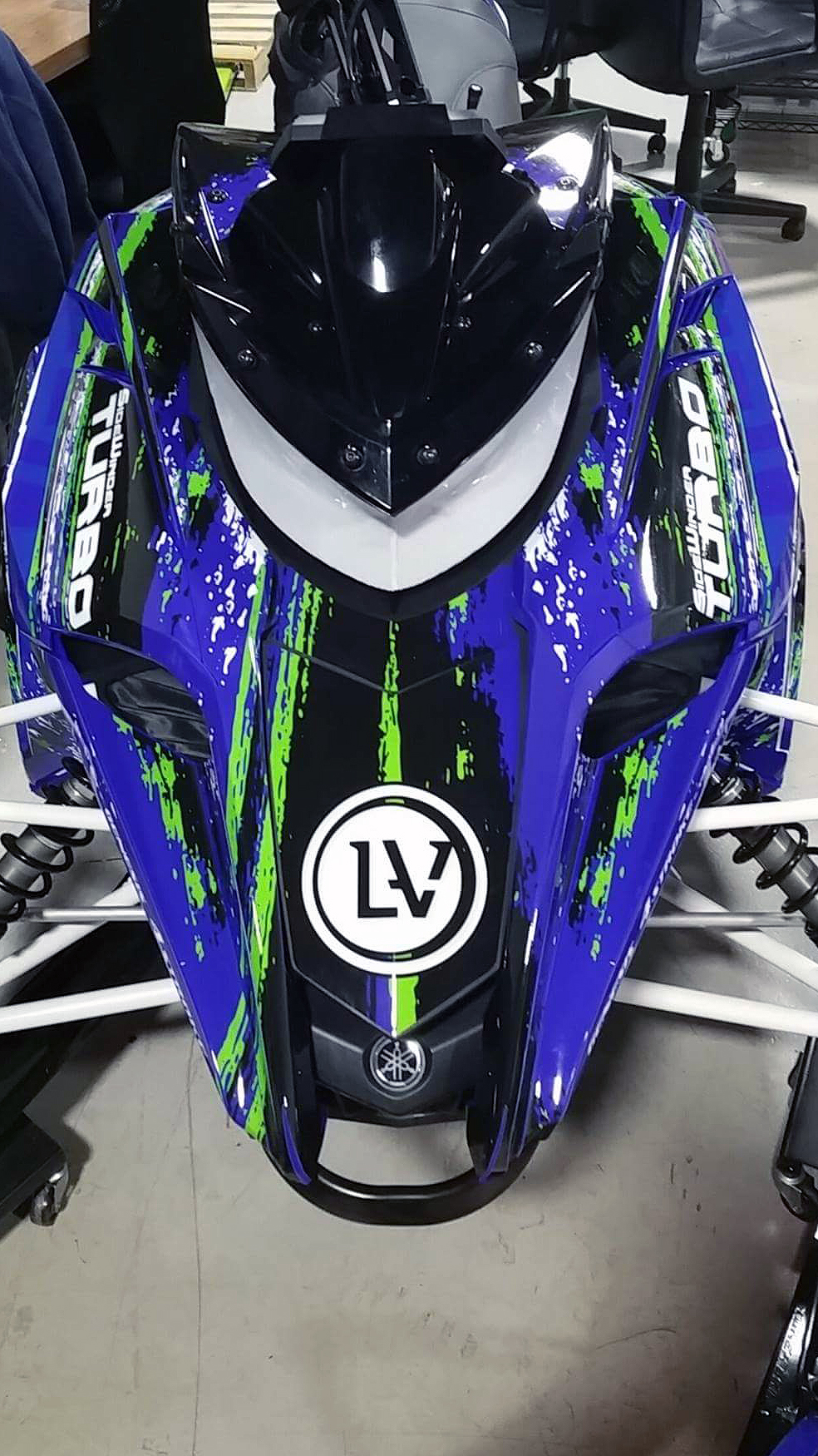 A Yamaha Sidewinder snowmobile with a blue, black, and green grunge lightning Infused custom vinyl wrap.