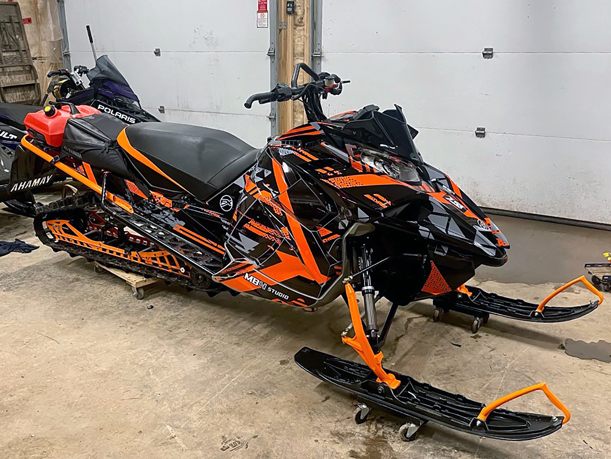 A Yamaha Sidewinder snowmobile with a orange, black, and gray MB4 Trifecta custom vinyl wrap.