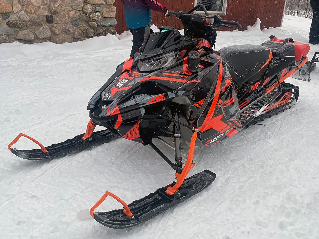A Yamaha Sidewinder snowmobile with a orange, black, and gray MB4 Trifecta custom vinyl wrap.
