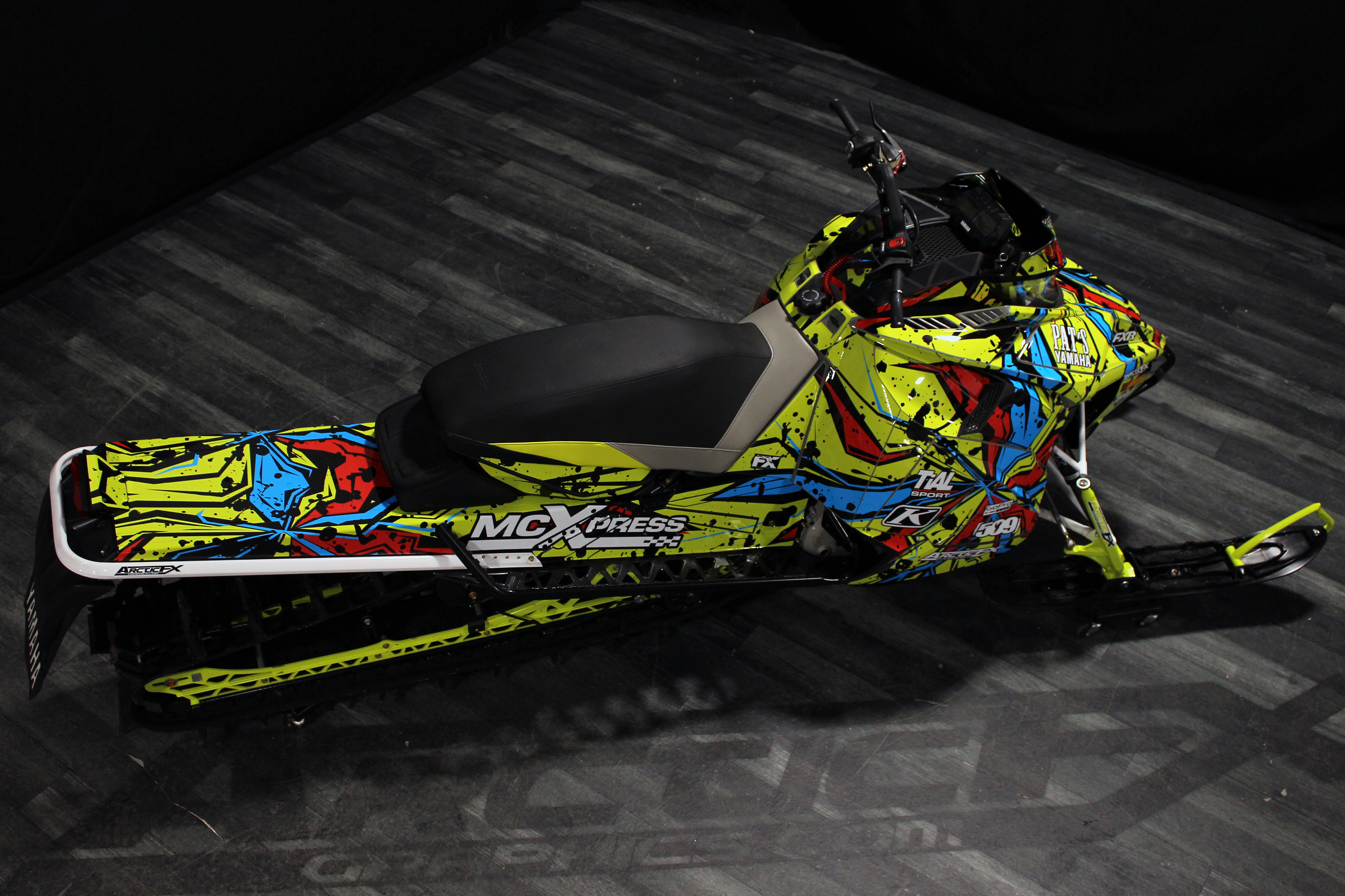 A Yamaha Sidewinder snowmobile with a lime squeeze, red, and black Stricken custom vinyl wrap.