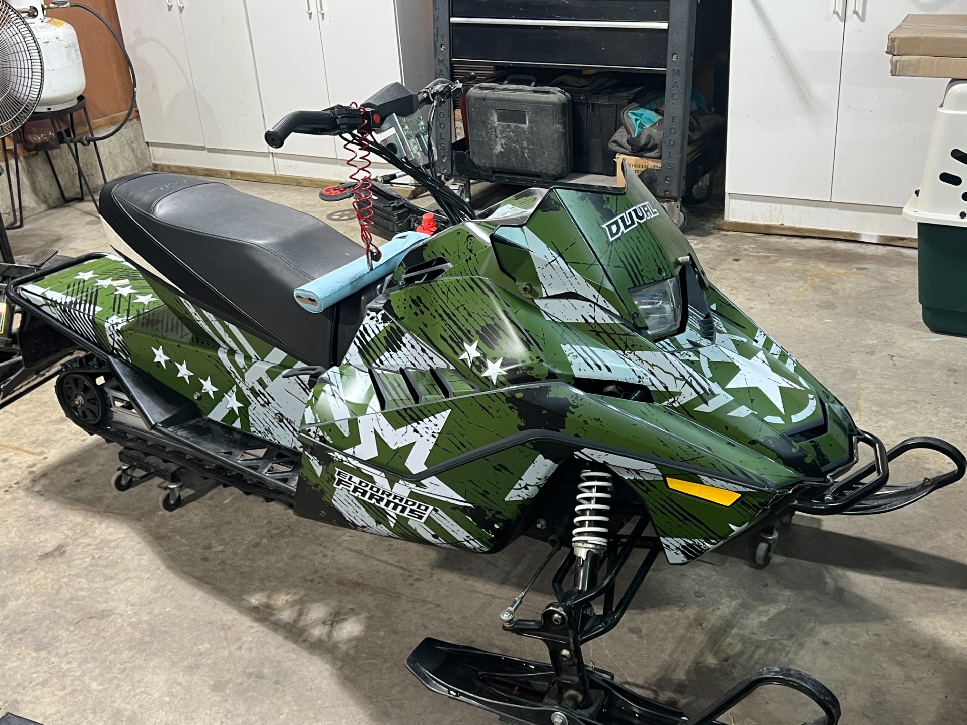 An Arctic Cat ZR200 youth snowmobile with a blue and green Wartorn custom vinyl wrap.