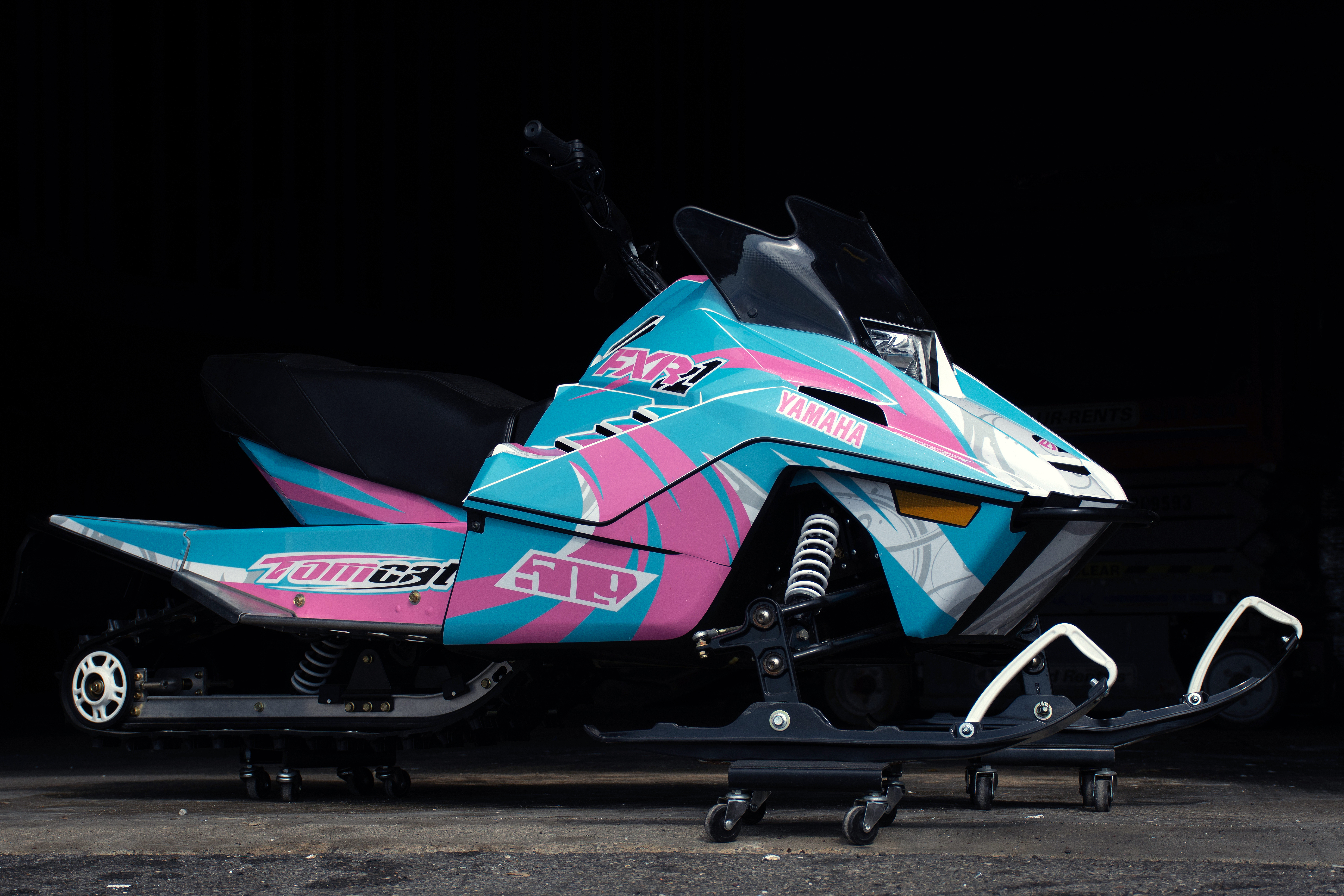 A Yamaha SnoScoot youth snowmobile with a white, pink, and blue Surge custom vinyl wrap.