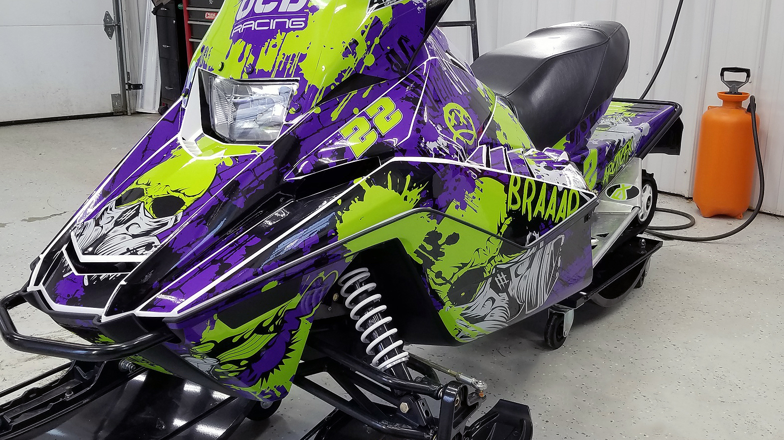 A Yamaha SnoScoot youth snowmobile with a purple, black, and lime Tagged custom vinyl wrap.