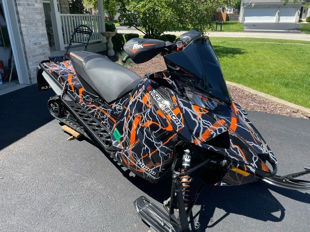 An ArcticCat Next-Gen snowmobile with a black, strike orange, and charcoal gray Hard Rain custom vinyl wrap.