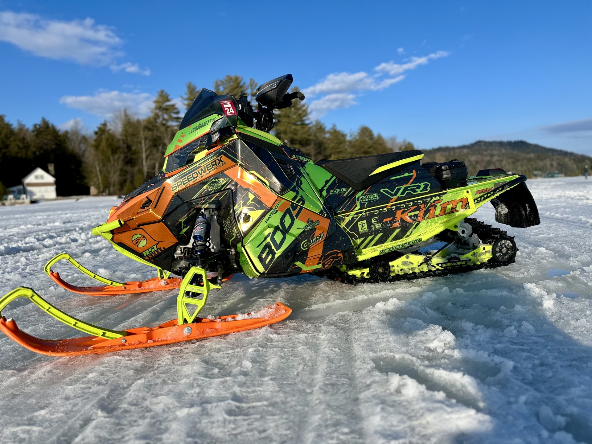 A Polaris Matryx Trail snowmobile with a gunmetal gray, orange, and hyper green KLIM Recoil wrap with chrome vinyl and halo flake laminate.