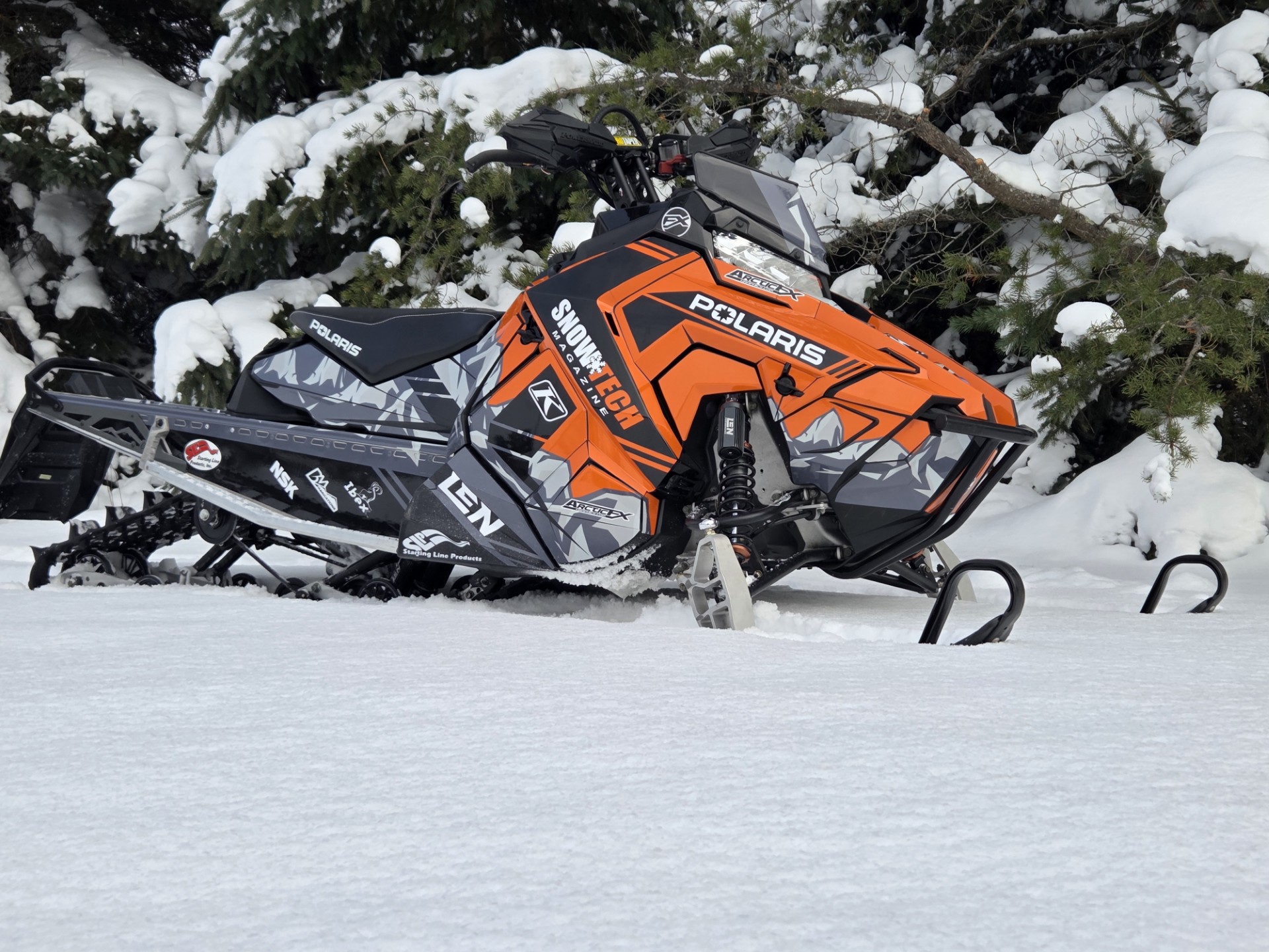 A Polaris Axys Trail snowmobile with a white, black, orange, ghost gray, light gray, and stealth gray Burandt Vista custom vinyl wrap.