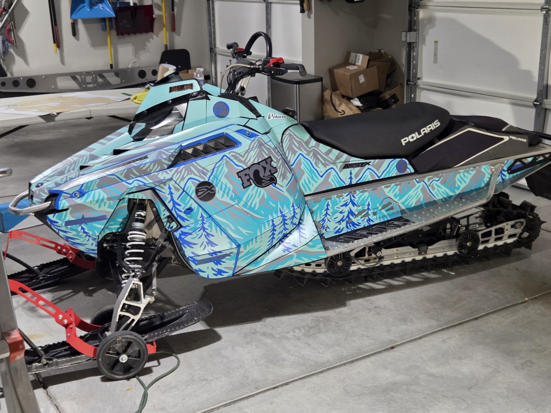 A Polaris ProRide snowmobile with a blue, asphalt gray, tiffany blue, monument gray, storm gray, and radiant green SledStar Conifer custom vinyl wrap with matte laminate.