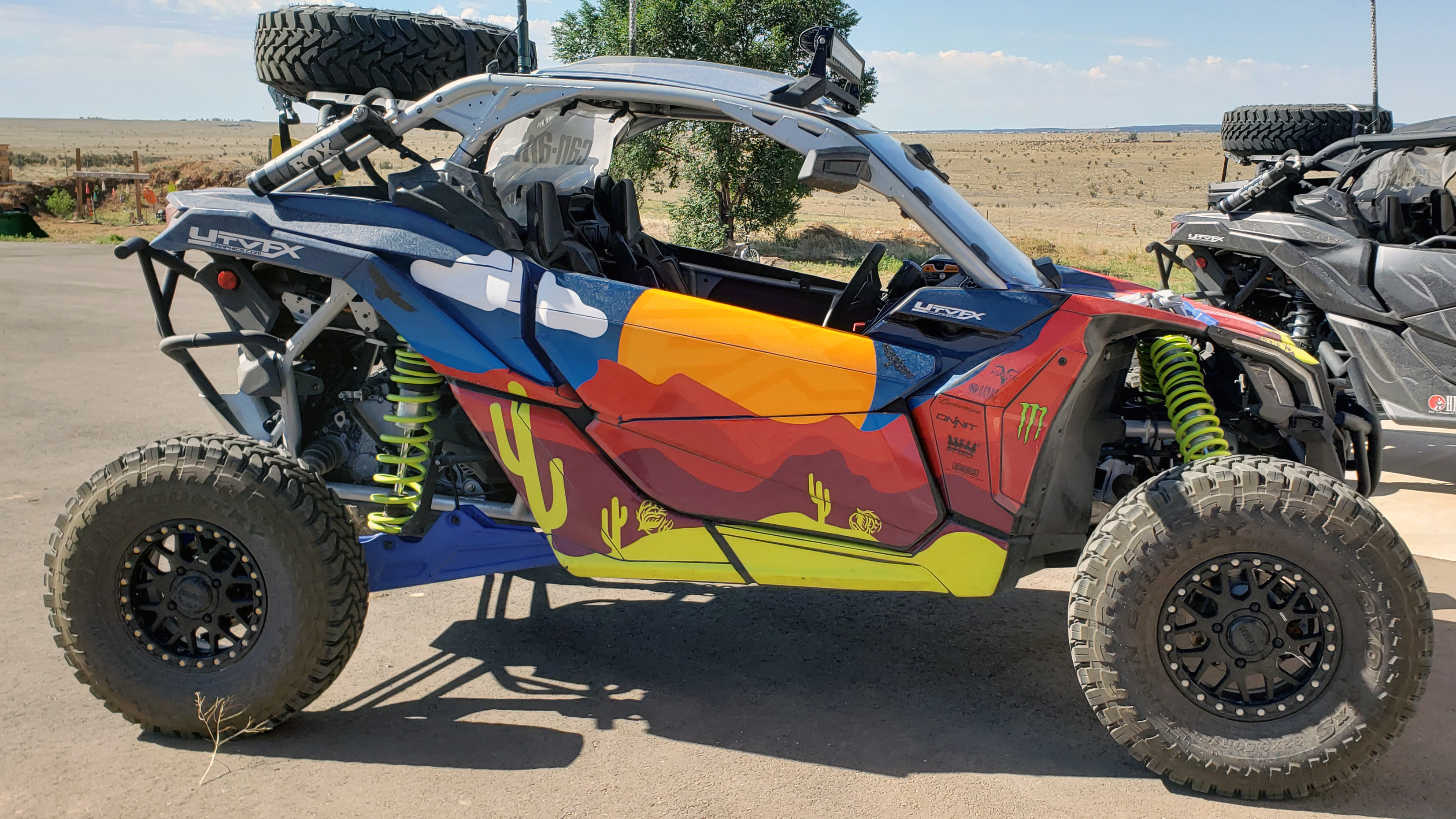 A Can-Am Maverick X3 side-by-side with a blue, red, and hi-vis cartoon desert Cowboy Cerrone UFC custom vinyl wrap.