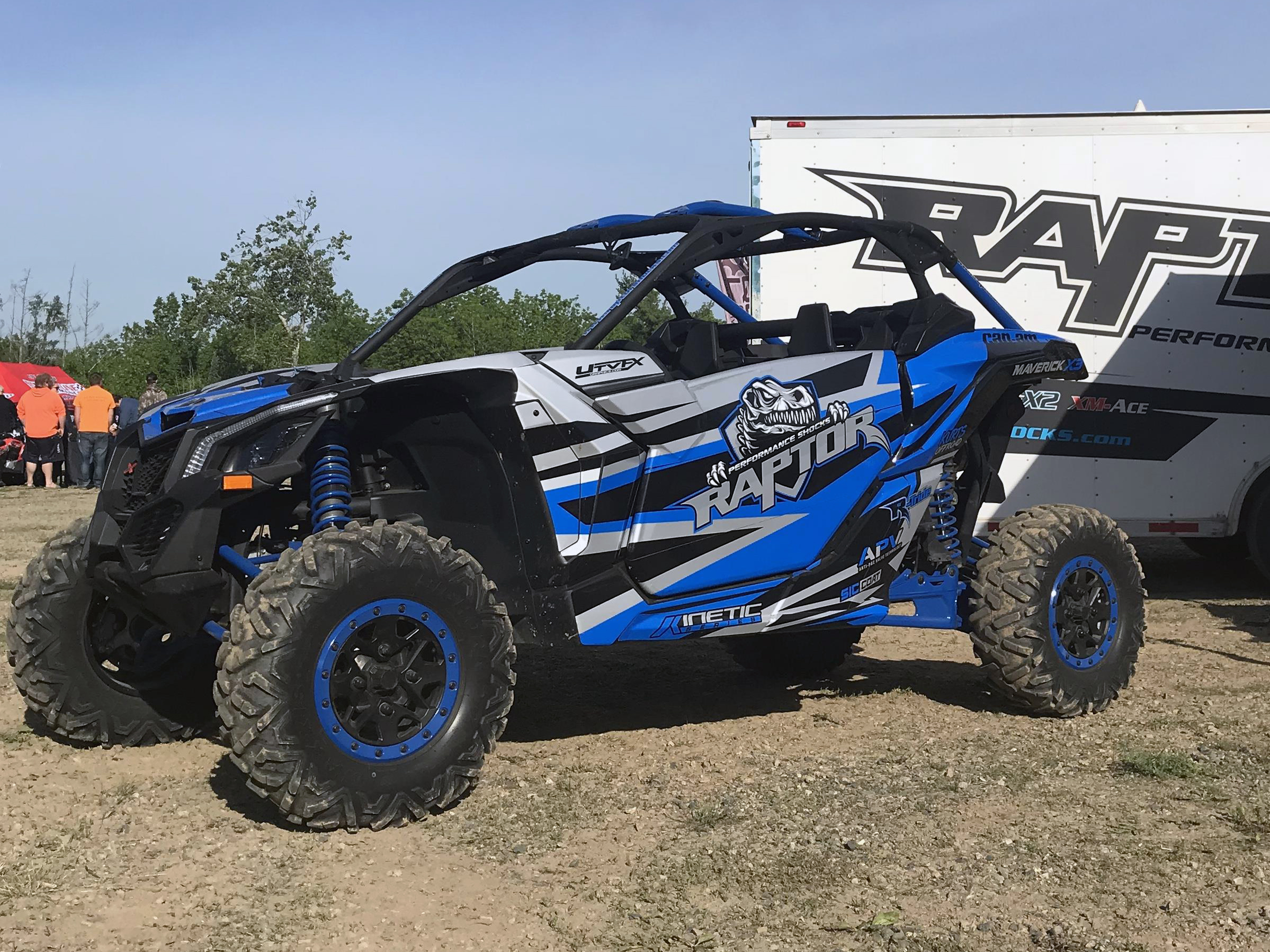 A Can-Am Maverick X3 side-by-side with a blue, black, and gray stripes Raptor Shocks custom vinyl wrap.