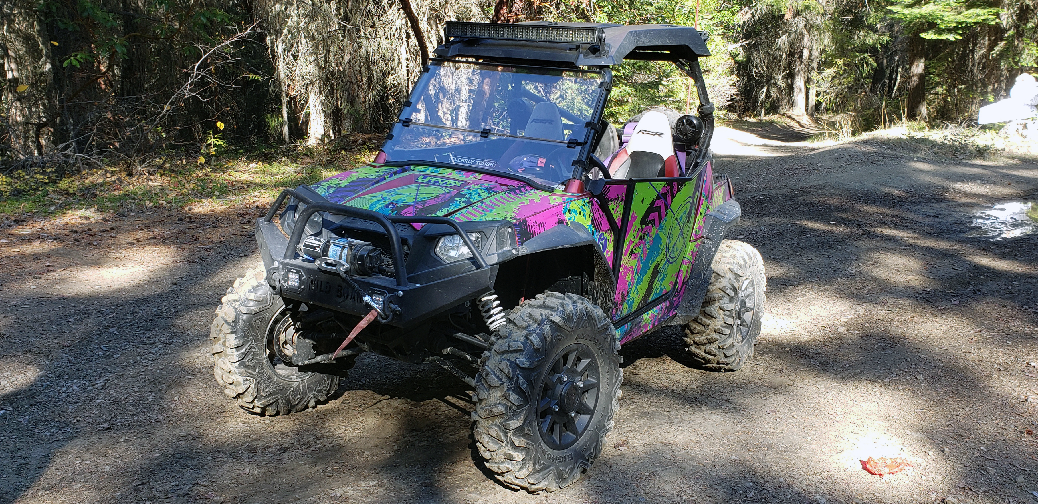 A Polaris RZR 2 Door side-by-side with a teal, green and pink Bombsquad custom vinyl wrap.