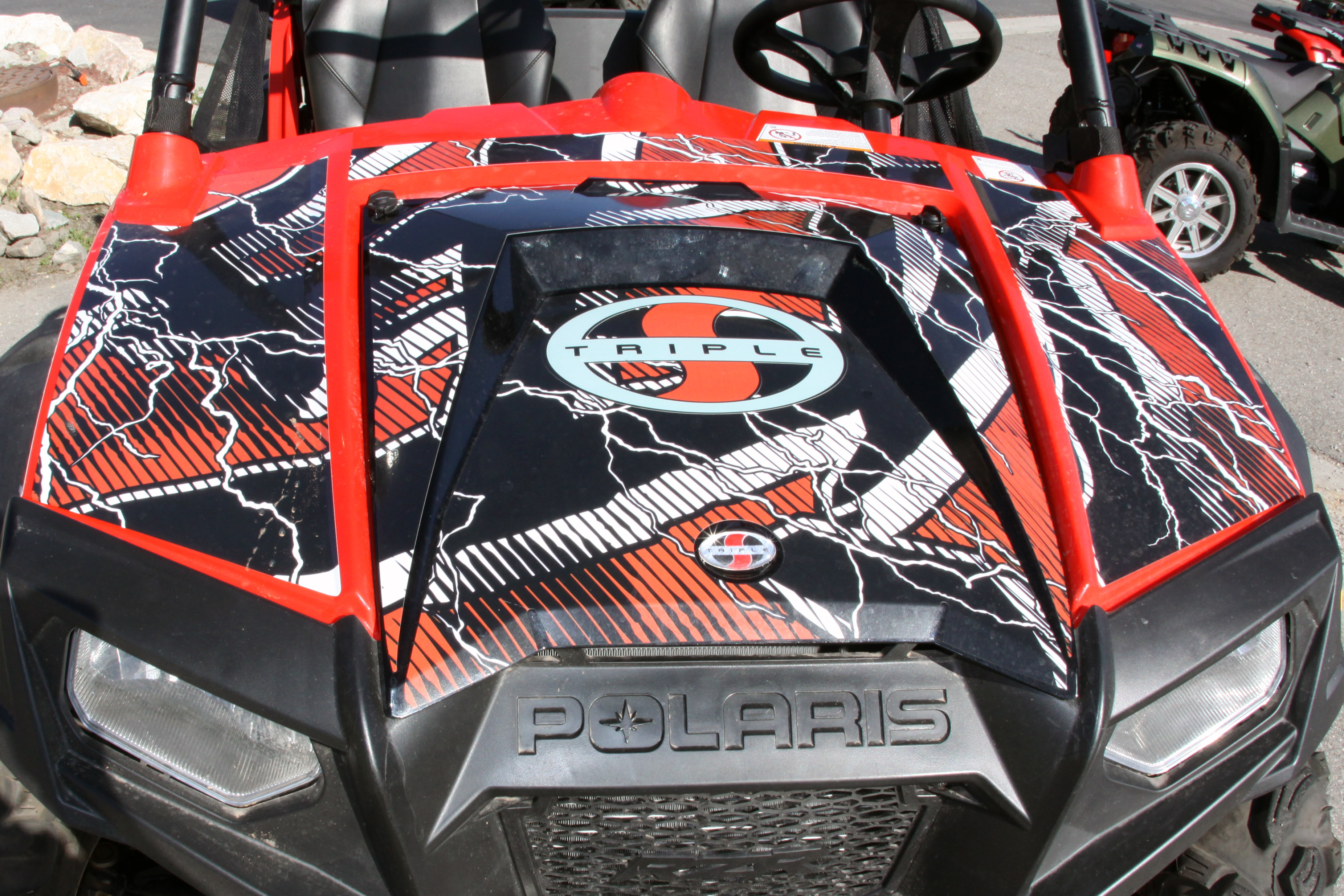 A Polaris RZR 2 Door side-by-side with a black, orange and white Hard Rain custom vinyl wrap.