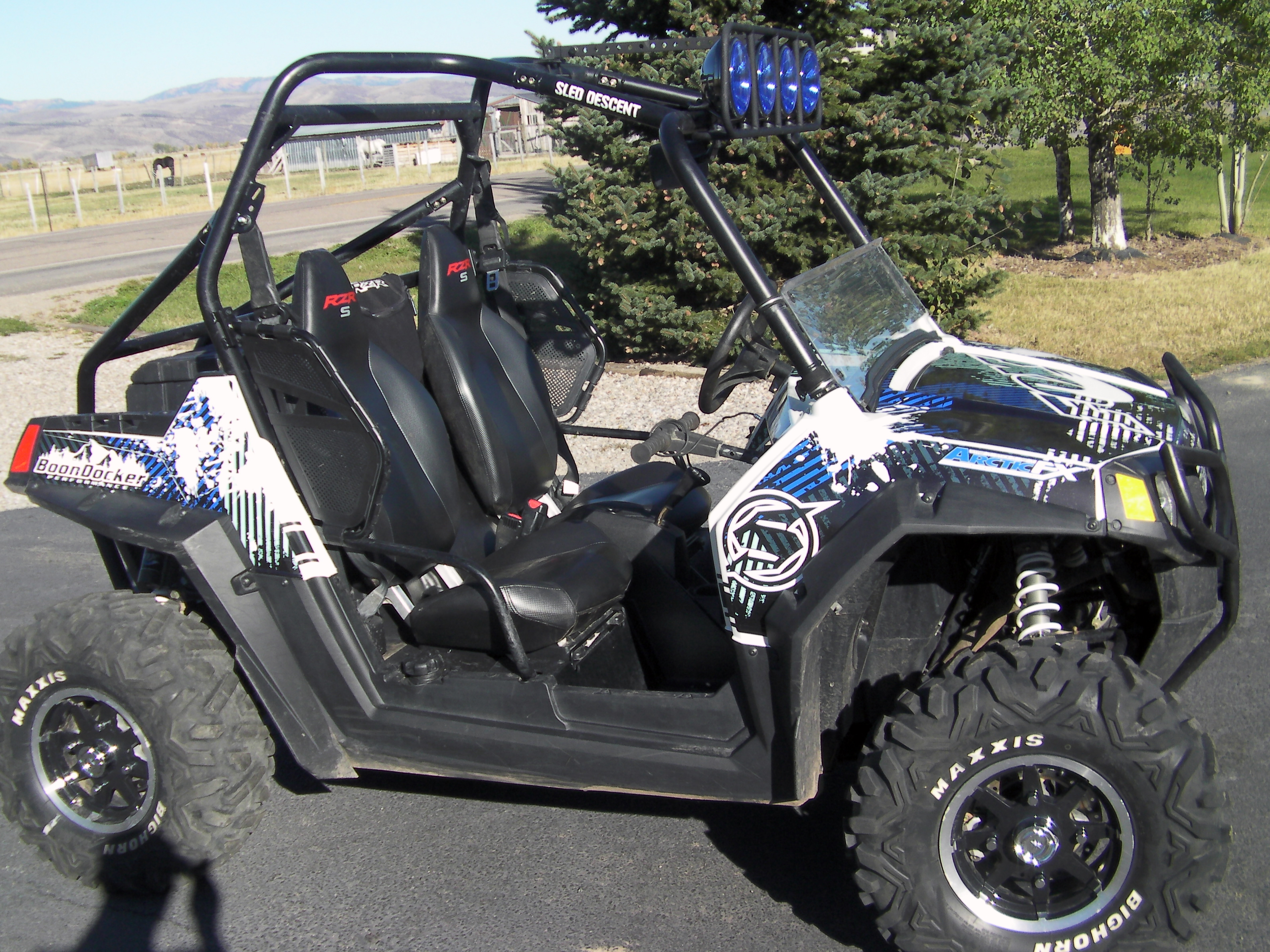 A Polaris RZR 2 Door side-by-side with a blue and white Point Blank custom vinyl wrap.