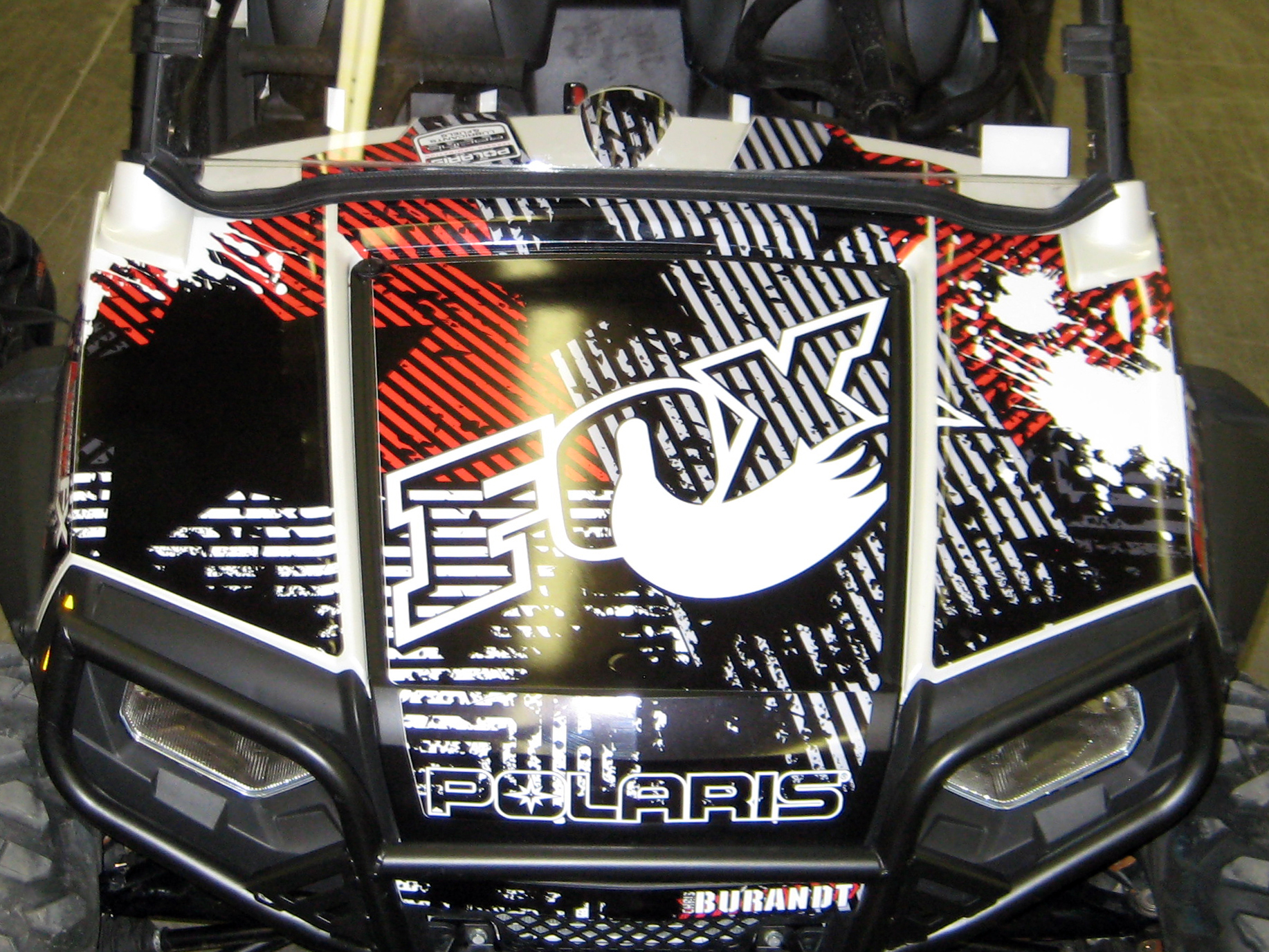 A Polaris RZR 2 Door side-by-side with a red and white Point Blank custom vinyl wrap.