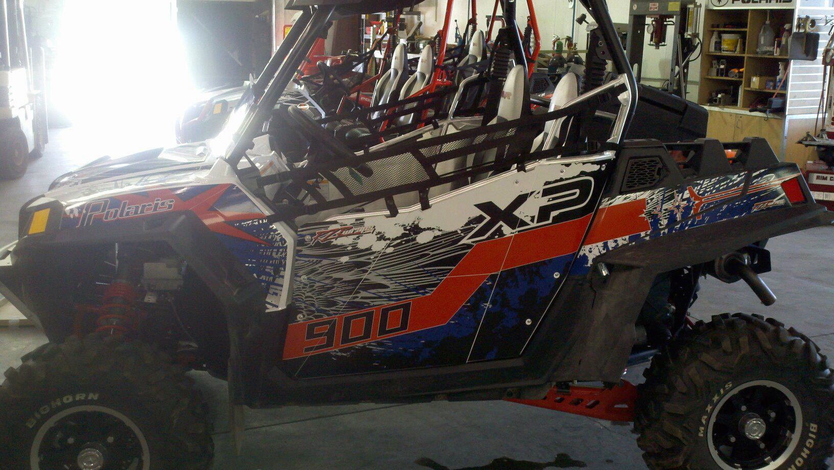 A Polaris RZR 2 Door side-by-side with a red and white Point Blank custom vinyl wrap.