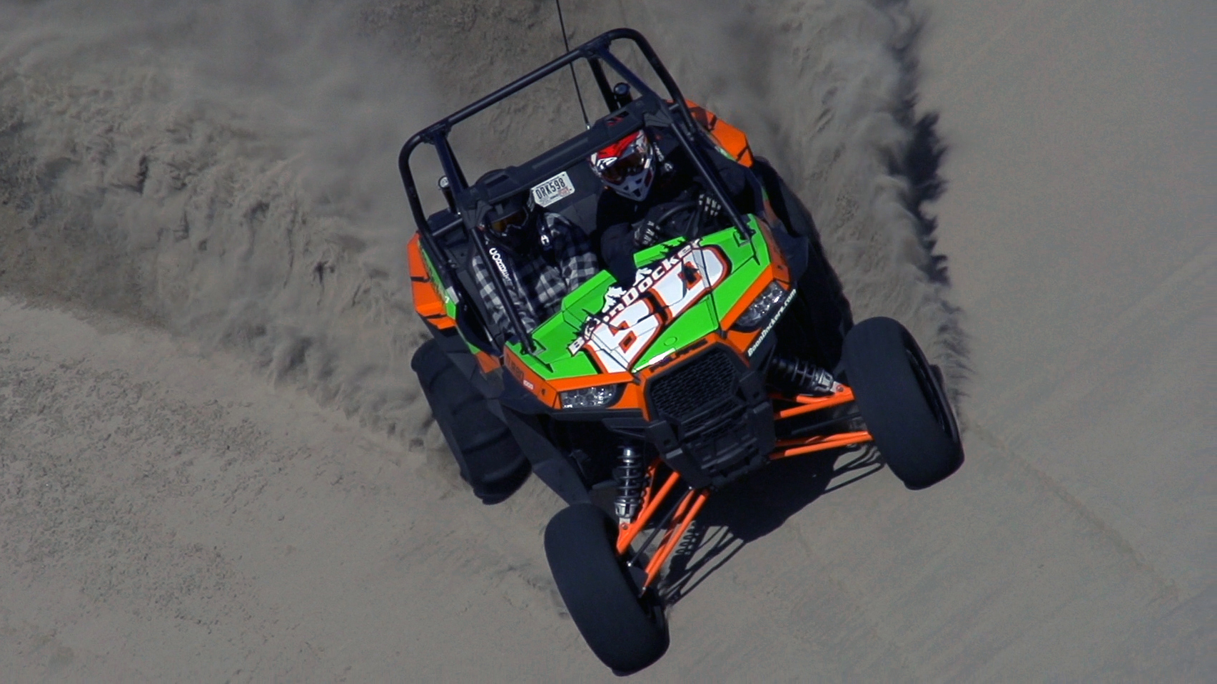 A Polaris RZR XP 2 Door side-by-side with a orange, green, black, and white stripes Boondocker Turbo custom vinyl wrap.