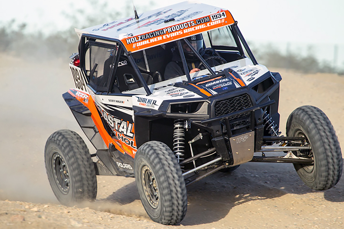 A Polaris RZR XP 2 Door side-by-side with a orange, white, and black Holz Racing custom vinyl wrap.