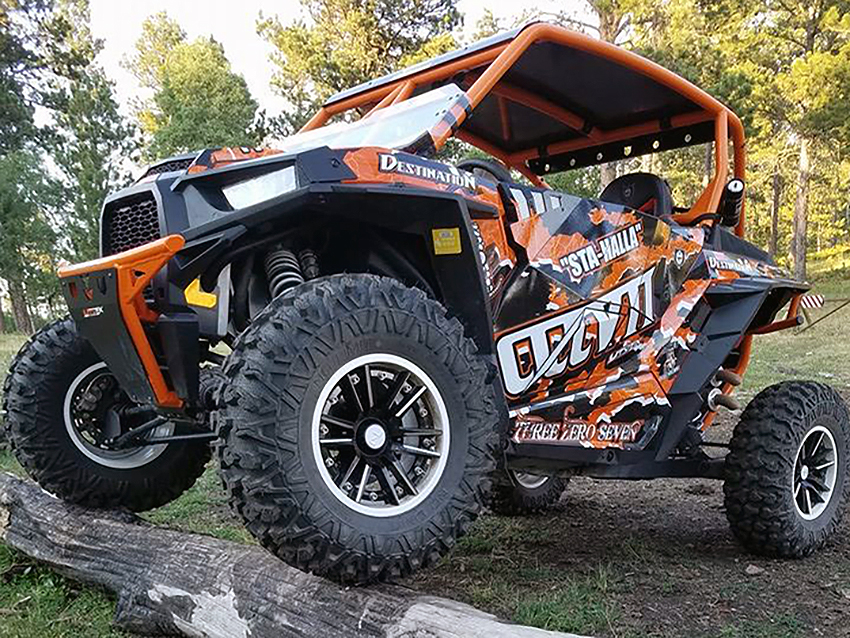 A Polaris RZR XP 2 Door side-by-side with a orange, black, and white grunge Shred custom vinyl wrap.