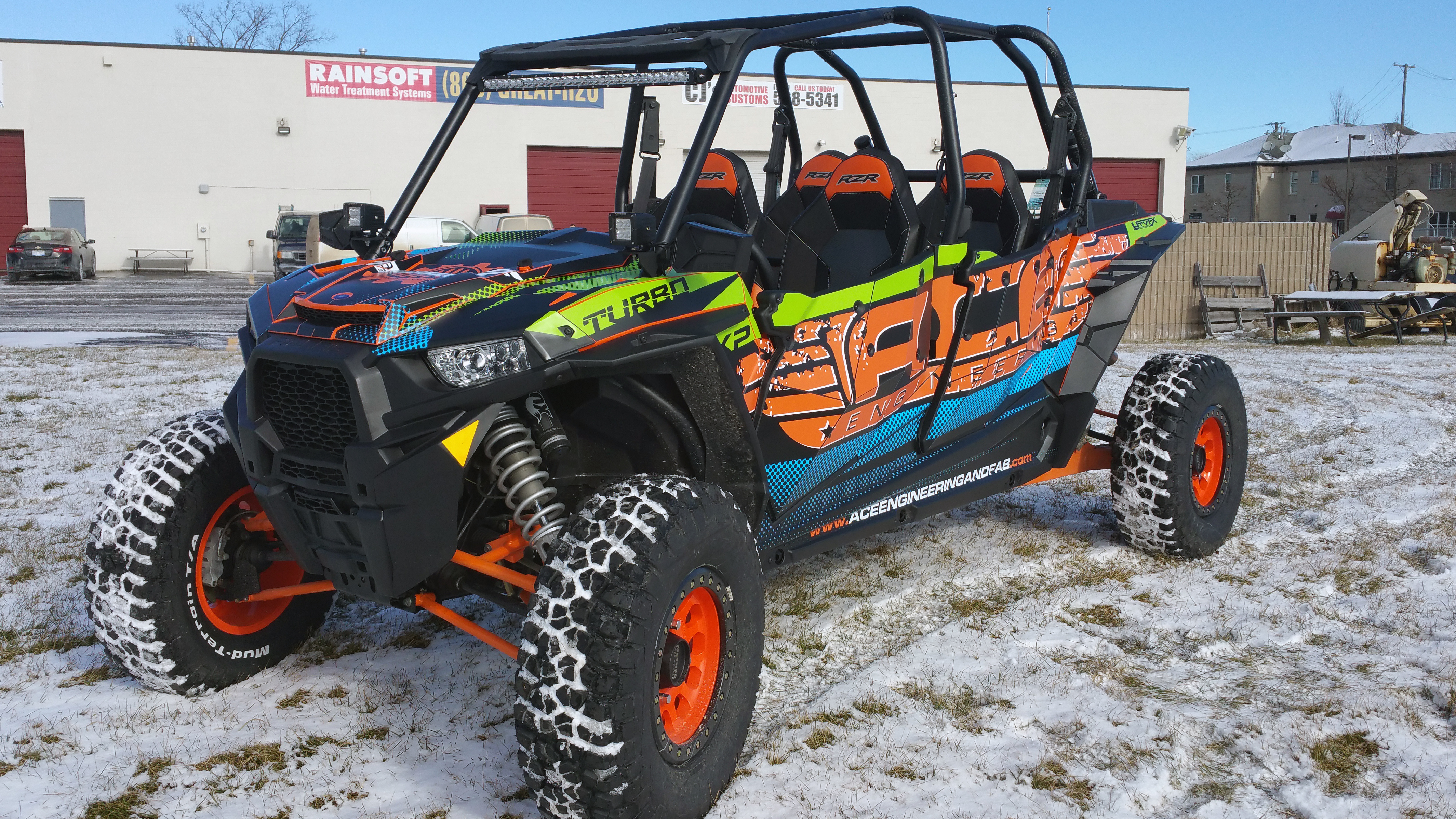 A Polaris RZR XP 4 Door side-by-side with a black, blue, green, and orange grunge Ace Engineering custom vinyl wrap.