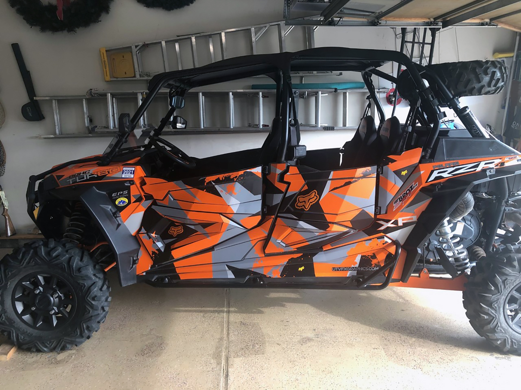 A Polaris RZR XP 4 Door side-by-side with a black, gray, and orange Klim Camo custom vinyl wrap.