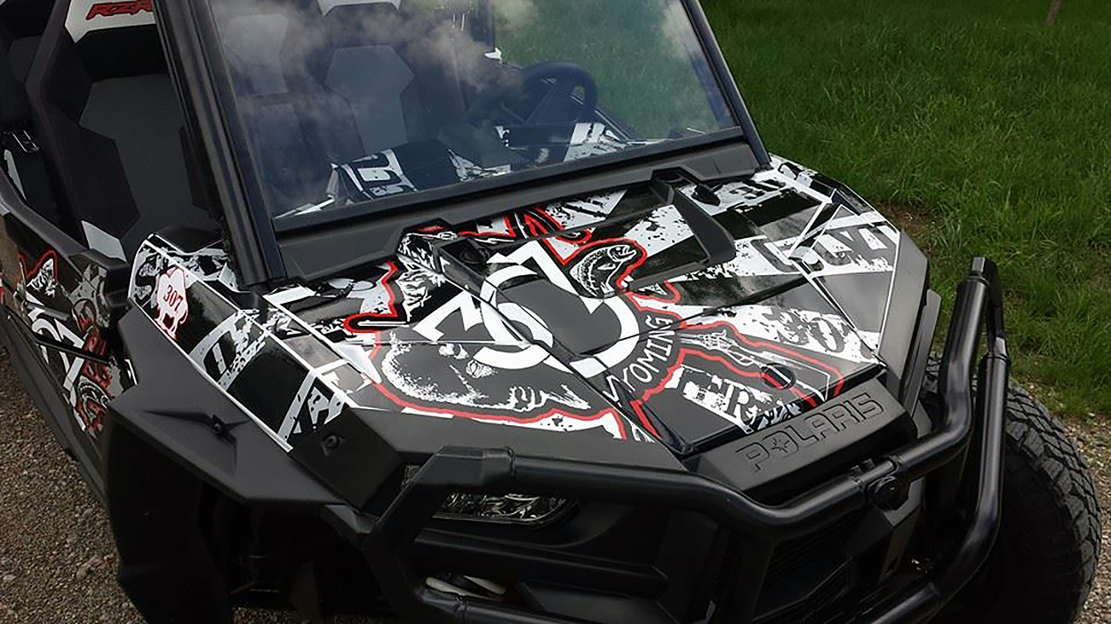 A Polaris RZR XP 4 Door side-by-side with a black, gray, and red grunge 307 Rising Sun custom vinyl wrap.